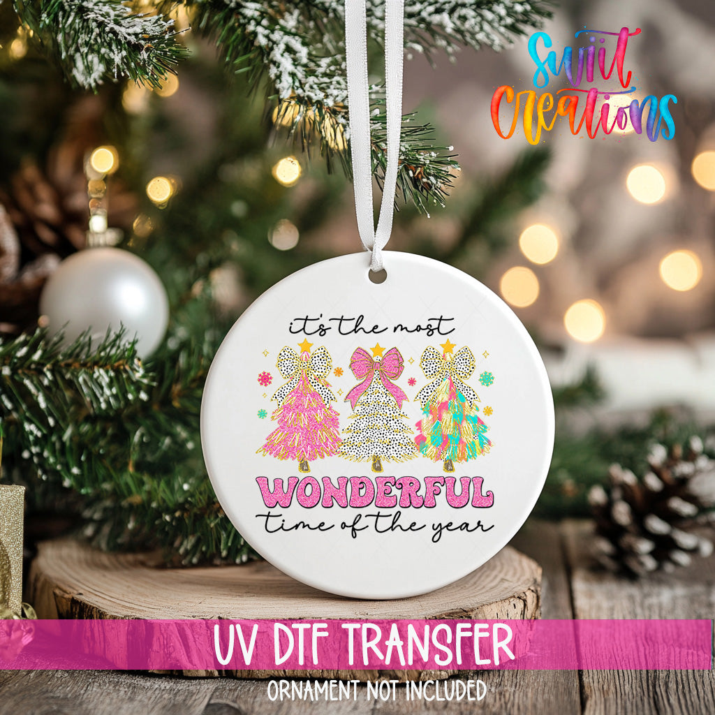 A white ceramic ornament with a festive design hangs on a Christmas tree, surrounded by pine branches and twinkling lights.