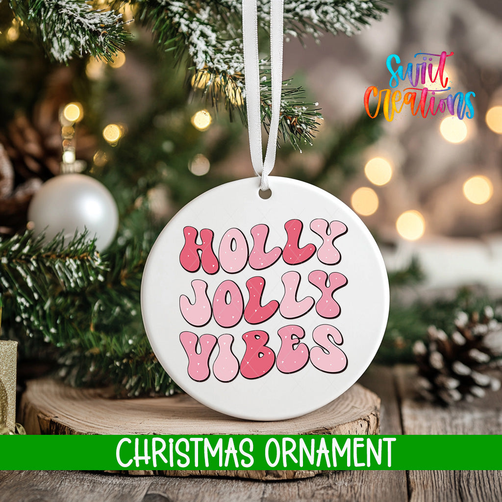 A white Christmas ornament with the text "Holly Vibes" in pink and red letters is hanging from a tree branch.
