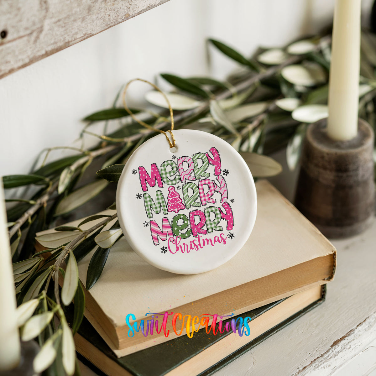 Round ceramic Christmas ornament featuring stacked patterned Merry Merry Merry Christmas lettering in pink and green, styled on books with holiday greenery
