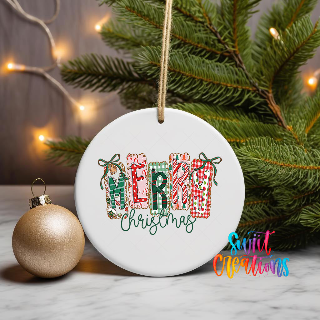 A white ceramic ornament with the word "MERRY CHRISTMAS" written on it, hanging from a string. The ornament is placed next to a gold ornament and a Christmas tree, creating a festive holiday scene.