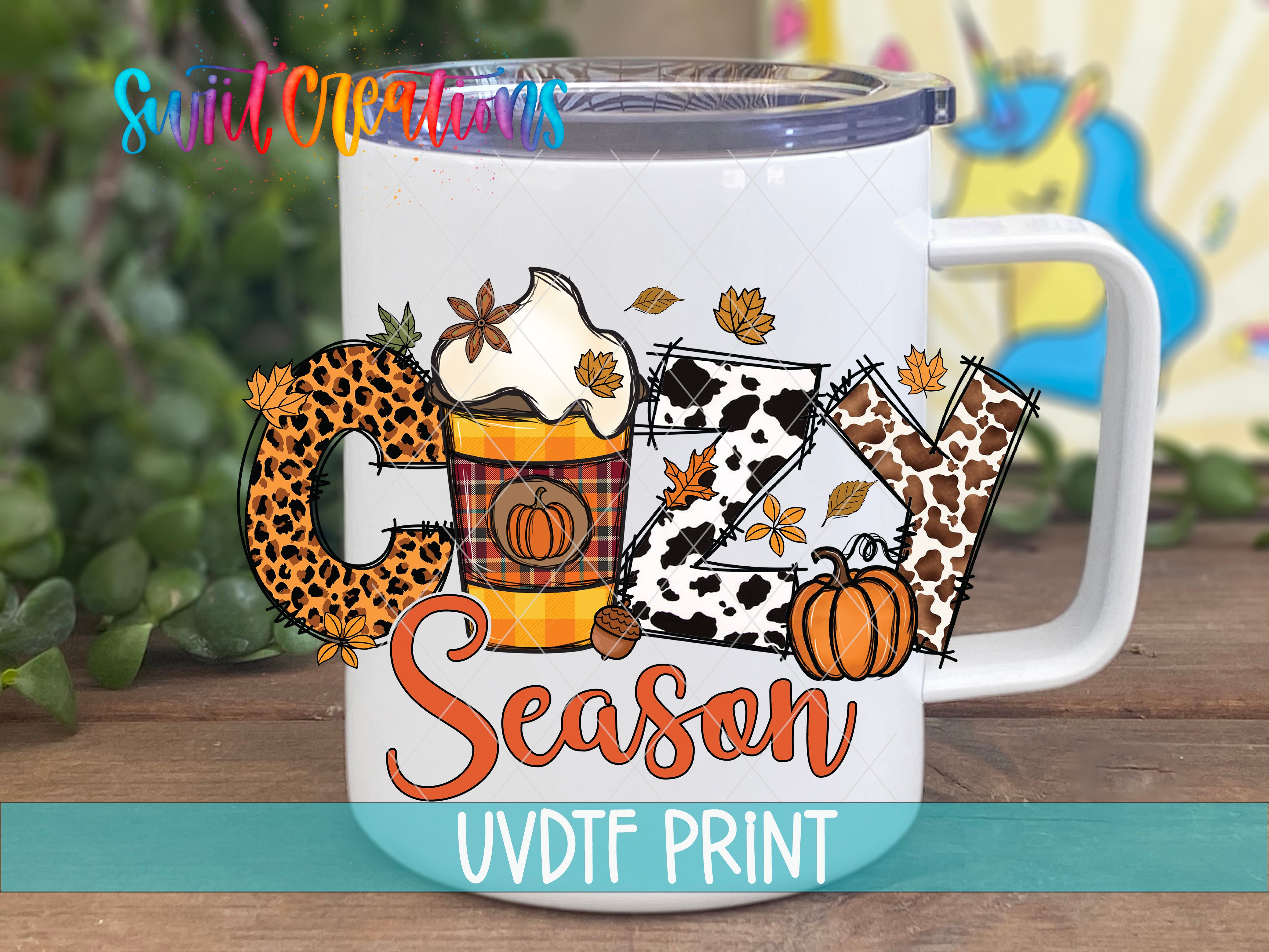 A white mug with a colorful design featuring the word "COZY" and various fall-themed elements such as leaves, pumpkins, and a leopard print pattern.