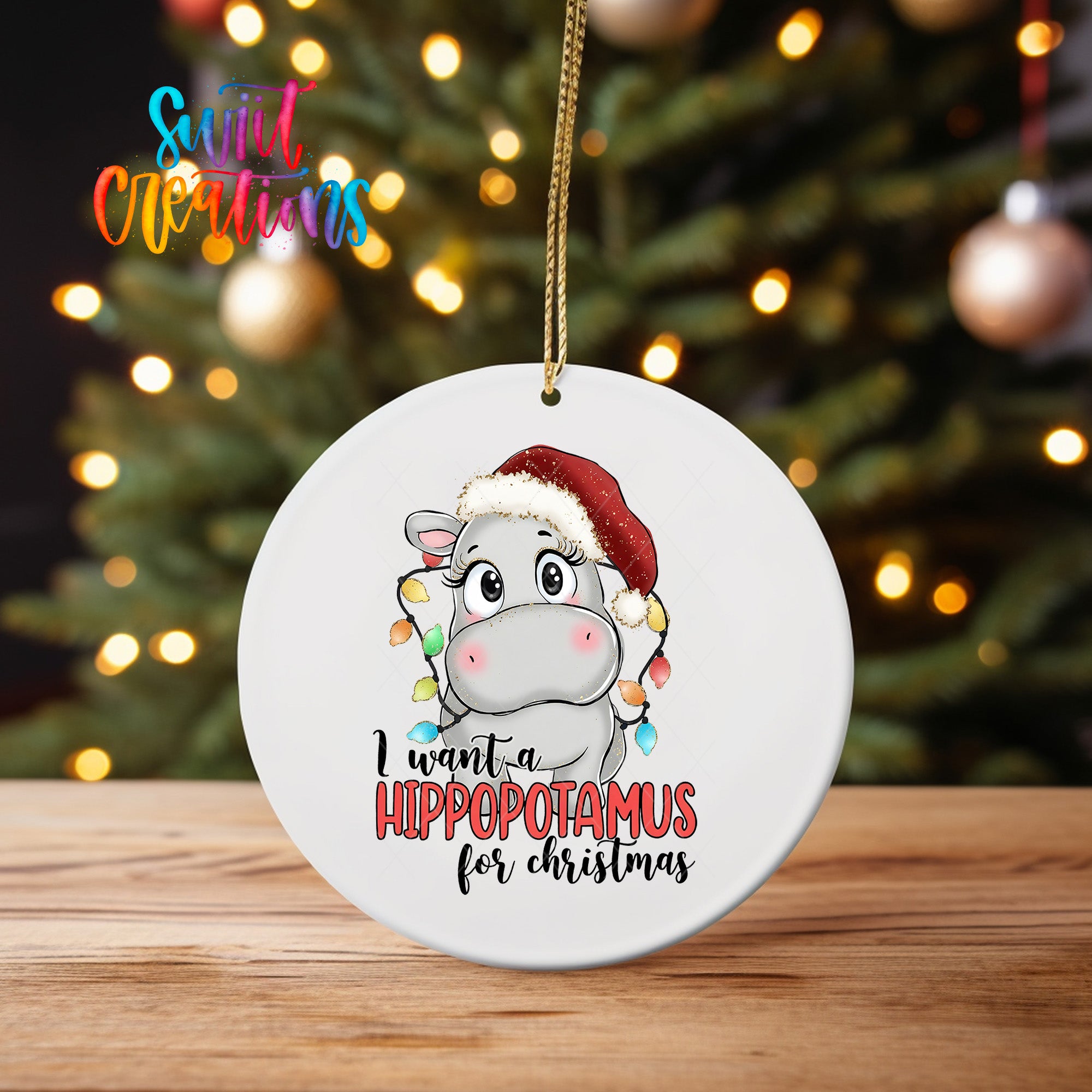 A white ceramic ornament with a cartoon image of a hippopotamus wearing a Santa hat and the text "I want a hippopotamus for Christmas" hanging from a string.