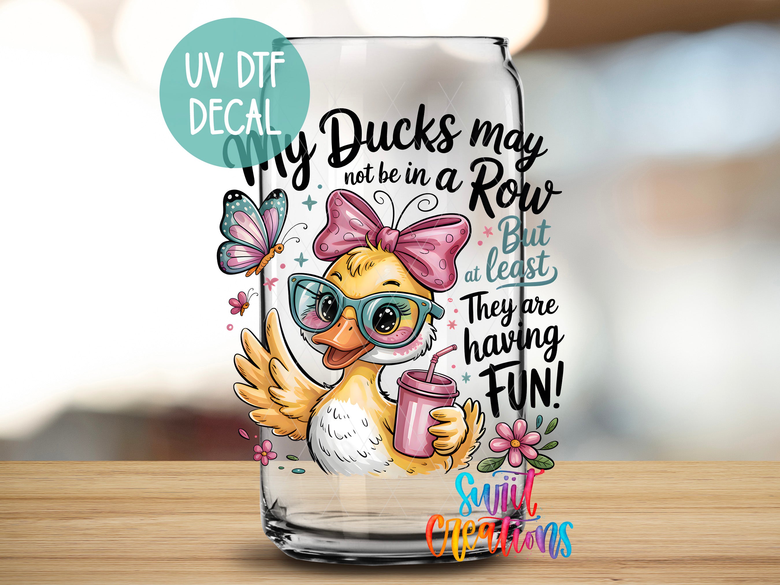 A glass jar with a cartoon duck wearing glasses and a bow, holding a drink, and surrounded by butterflies and flowers. The text on the jar includes phrases such as "My Ducks may not be in a Row", "But at least", "They are having Fun!", and "Sunlit Occasions".