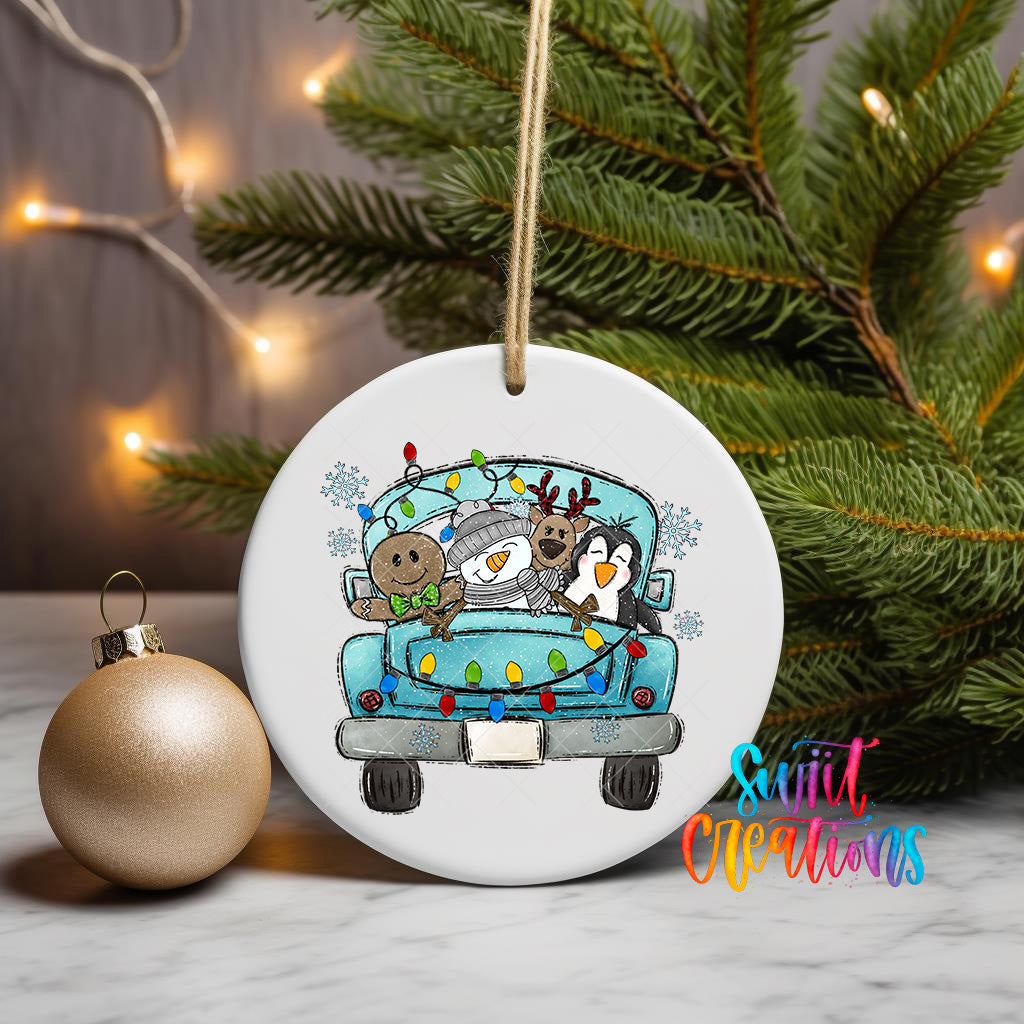 A white ceramic ornament featuring a cartoon illustration of a truck with a penguin, reindeer, and gingerbread man, along with Christmas lights. The ornament is hanging on a wall, and there is a gold ornament next to it.
