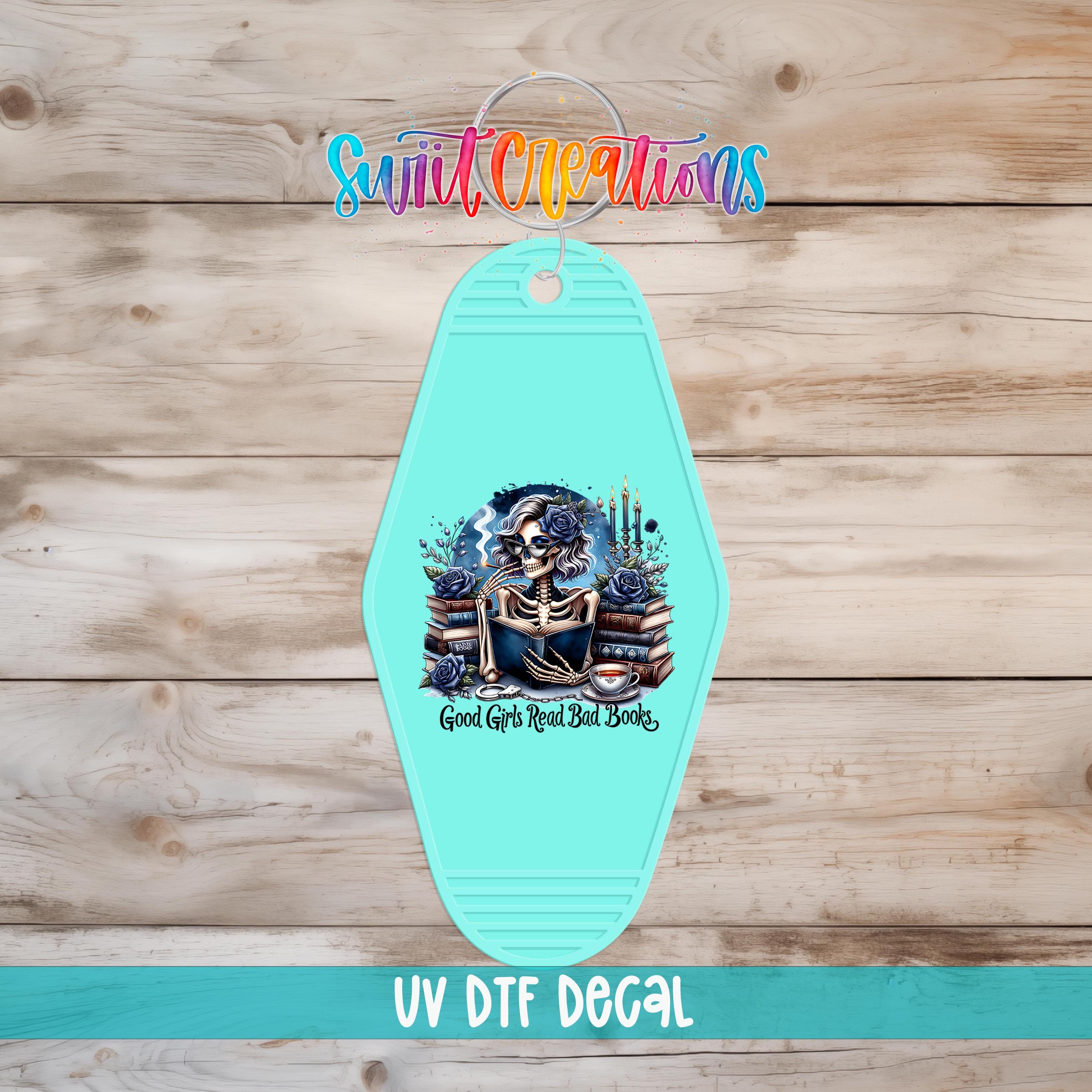 A turquoise keychain with a skull and crossbones design, along with the text "Good Girl Read Bad Books" printed on it.