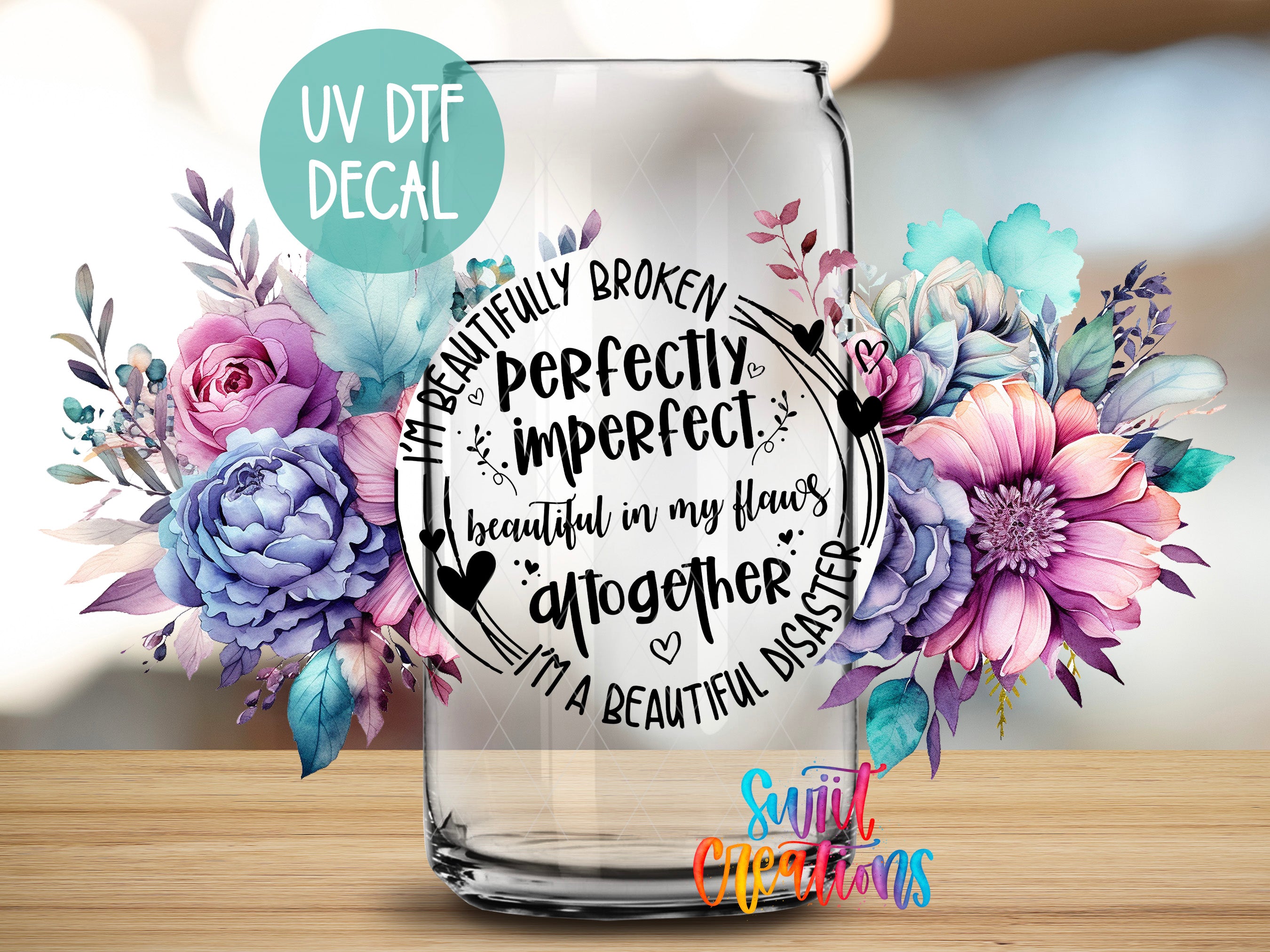 a glass jar with a floral design and text inside it, placed on a wooden surface.