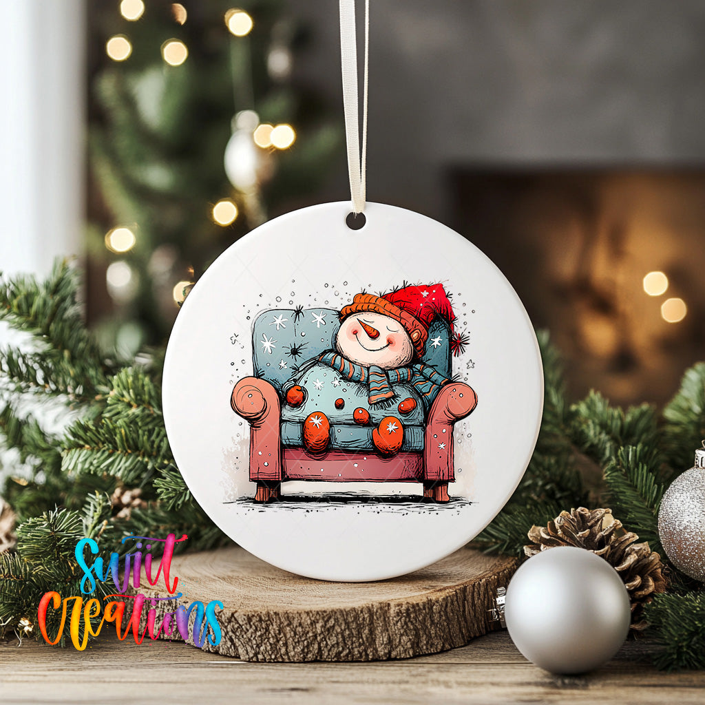 A white ceramic ornament featuring a snowman sitting in a red armchair, surrounded by Christmas decorations and greenery.