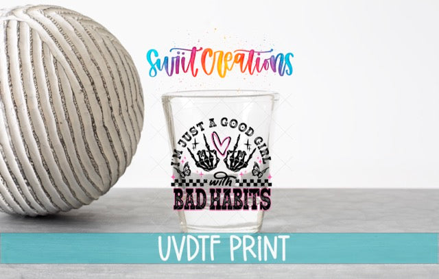 a shot glass with a hand-drawn design and text, placed next to a white ball on a gray surface.