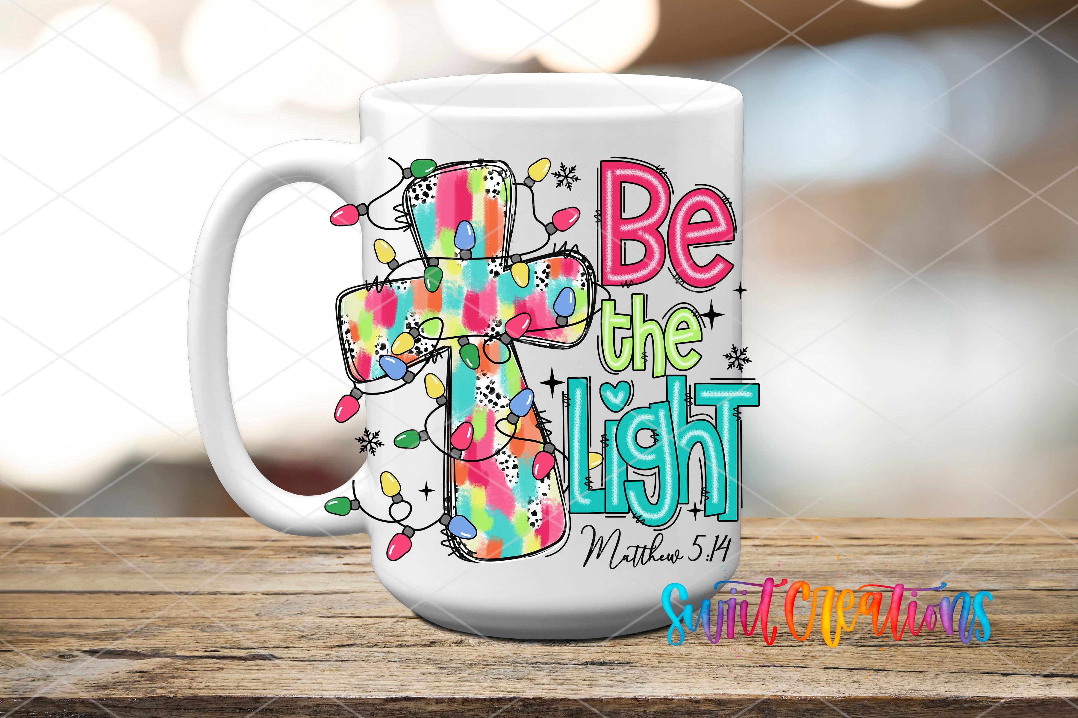 A white ceramic mug with a colorful design featuring a cross and Christmas lights, along with the text "Be the light" and "Matthew 5:14".