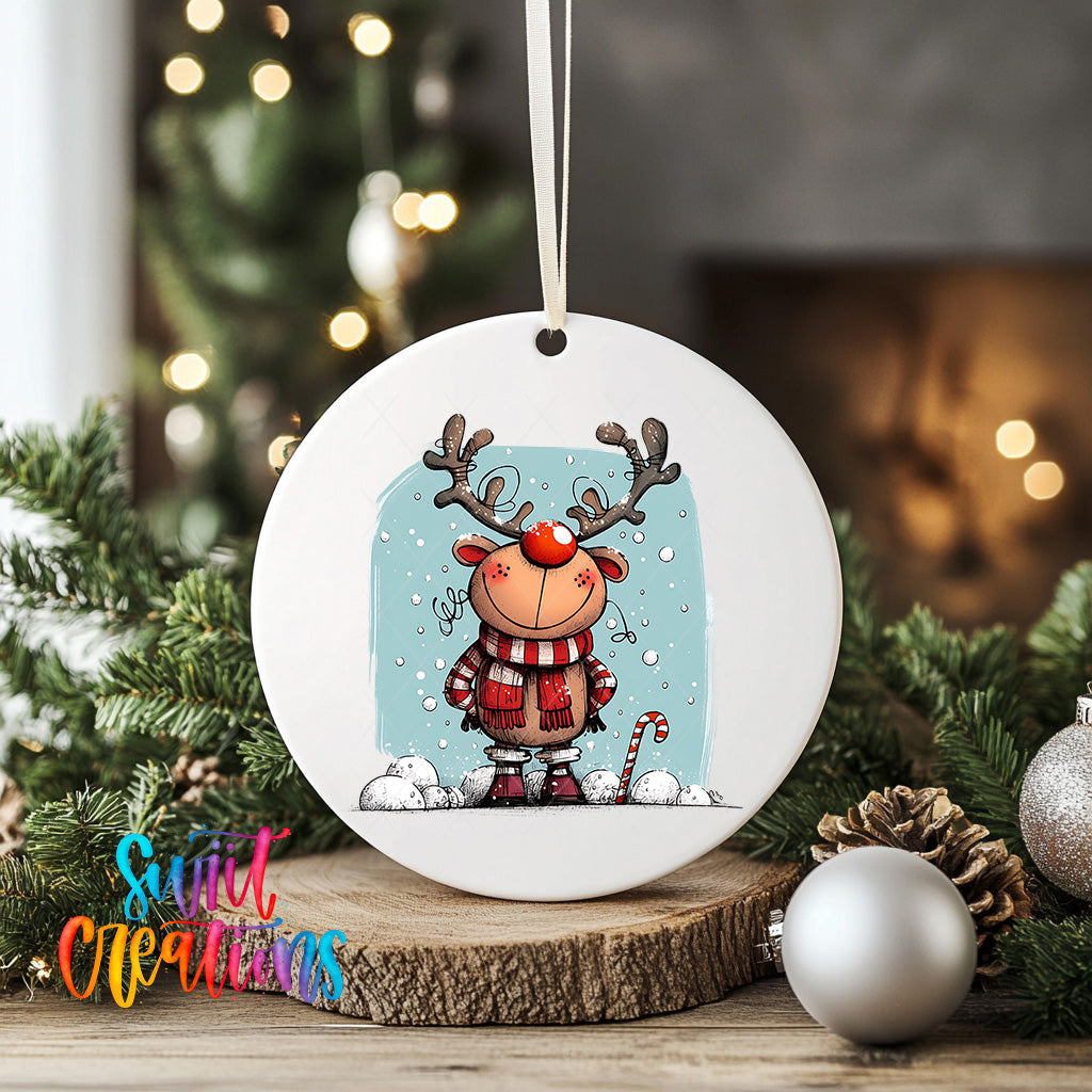 A white ceramic ornament featuring a cartoon reindeer with antlers, wearing a red scarf and standing on a snowy surface, surrounded by Christmas decorations and ornaments.