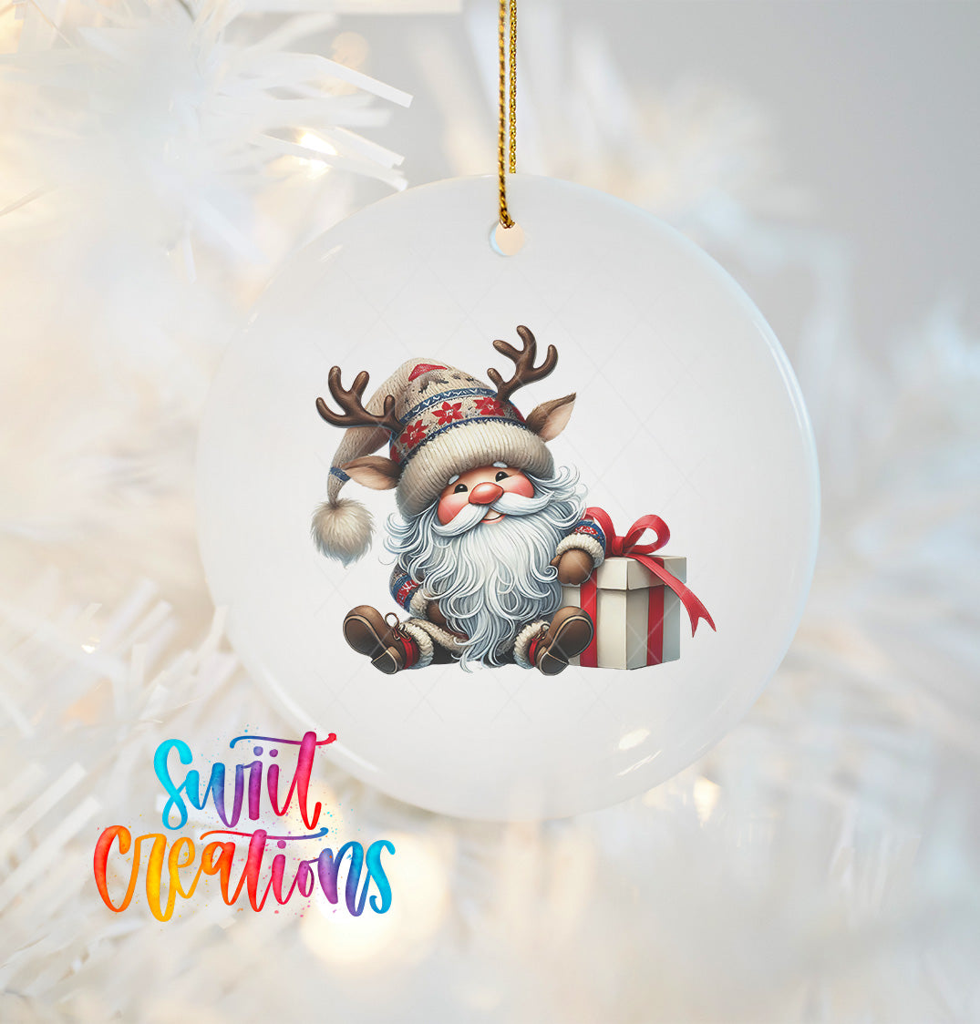 A white ornament with a Santa Claus figure and a gift box, hanging on a Christmas tree.