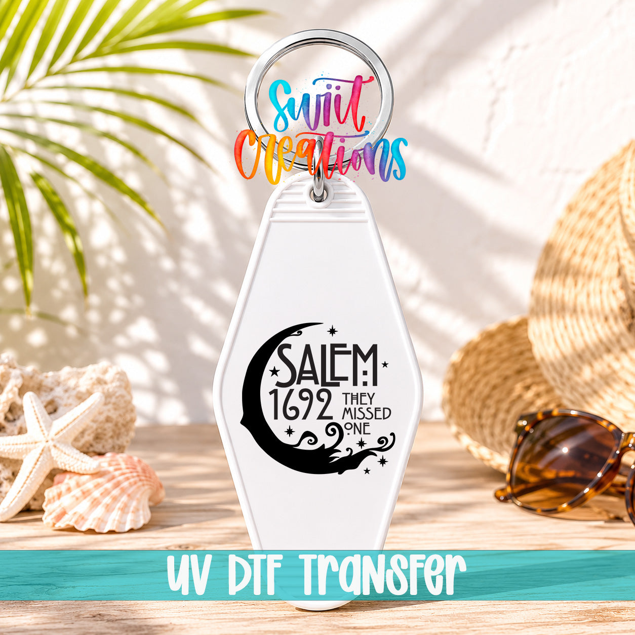A keychain with a crescent moon design and text, placed on a wooden surface with sunglasses and a straw hat in the background.