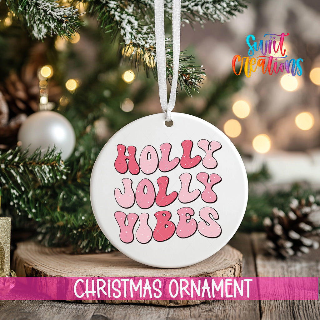 A white Christmas ornament with the text "Holly Vibes" in pink and red letters is hanging from a tree branch.