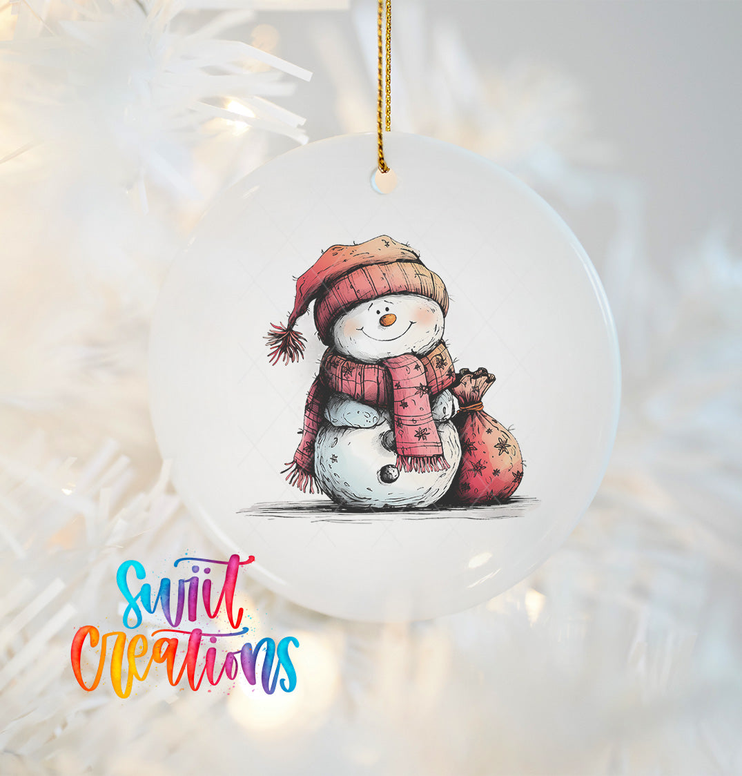A white ornament with a snowman illustration on it, hanging on a Christmas tree.