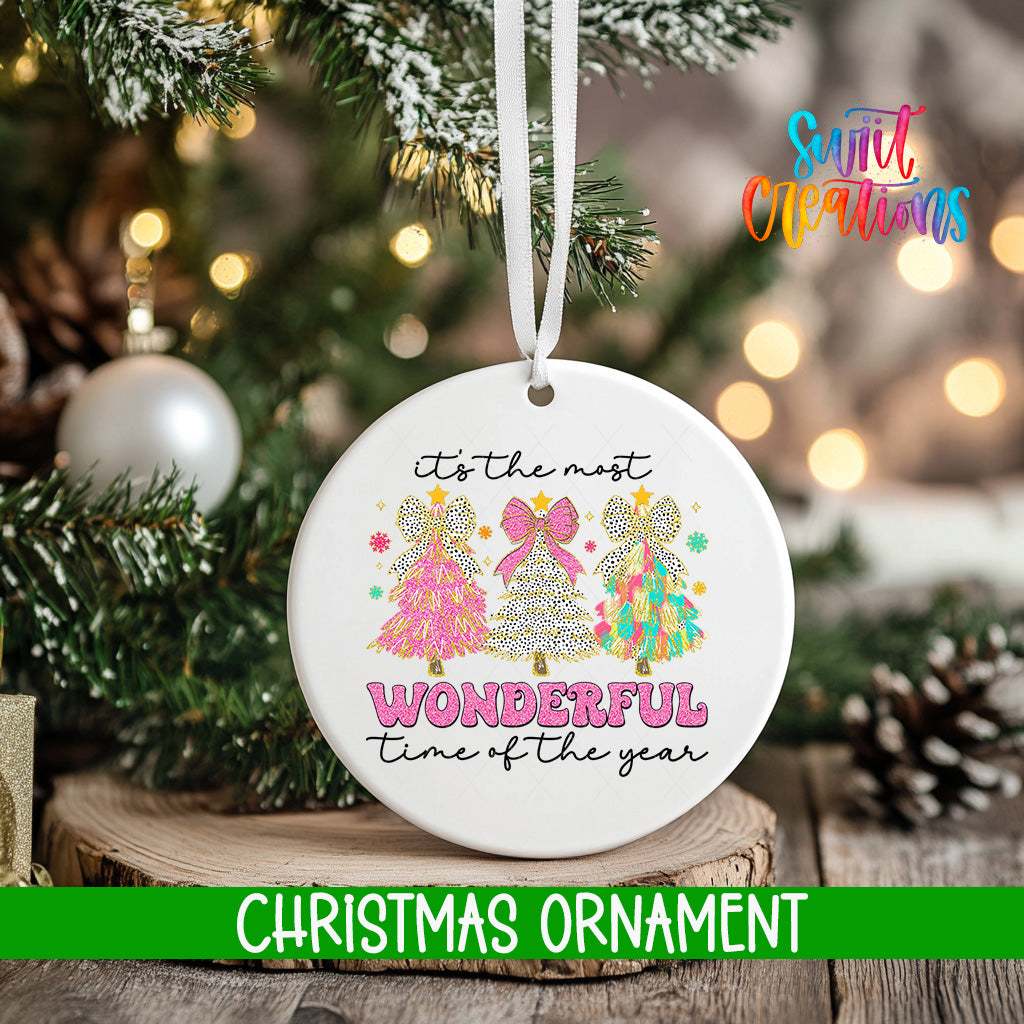 A white Christmas ornament with a design of three colorful Christmas trees and the text "It's the most wonderful time of the year" hanging from a string.