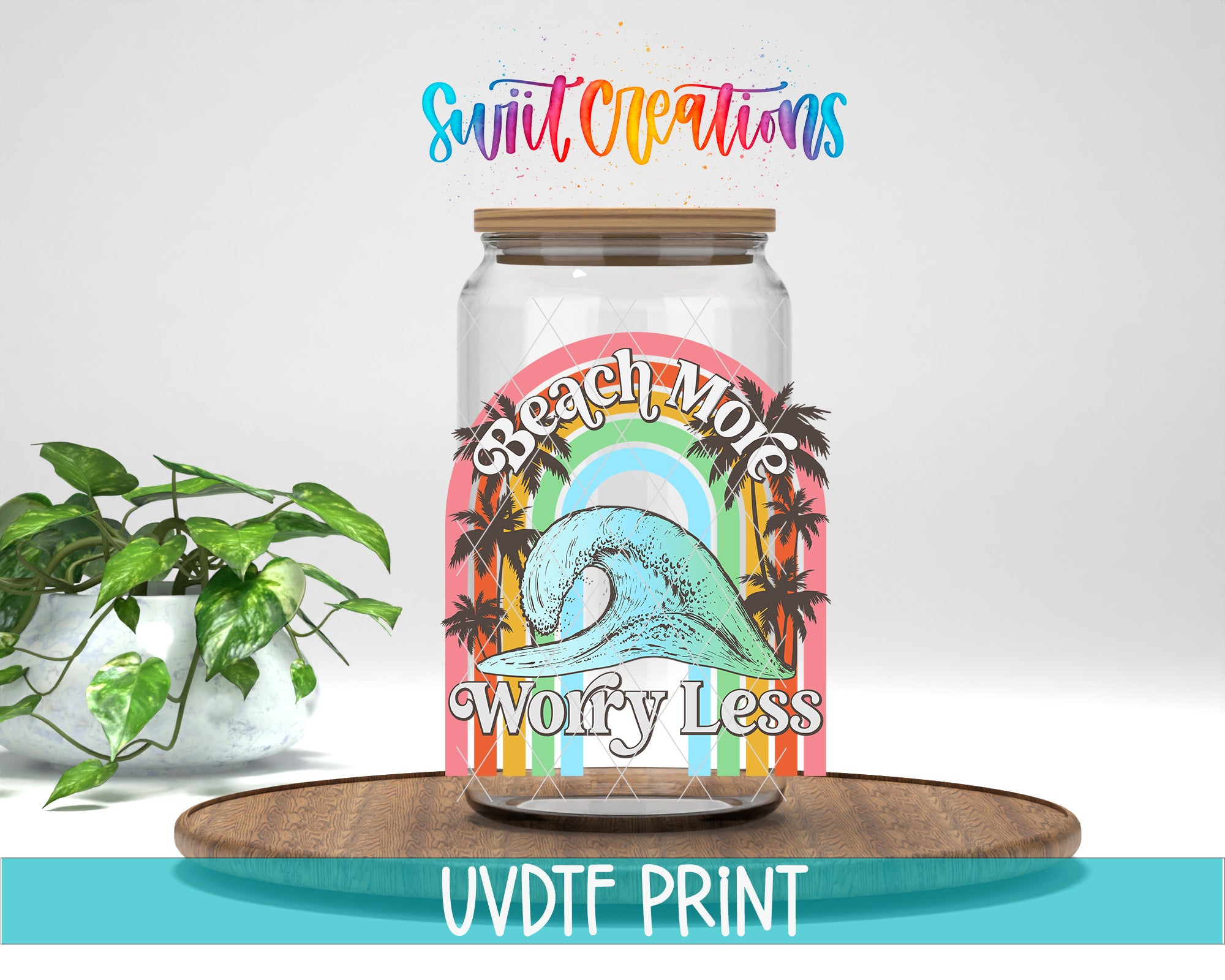 A glass jar with a colorful design featuring a wave and palm trees, along with the text "Beach More Worry Less" and "Swift Creations" written above it. The jar is placed on a wooden surface, and there is a potted plant in the background.