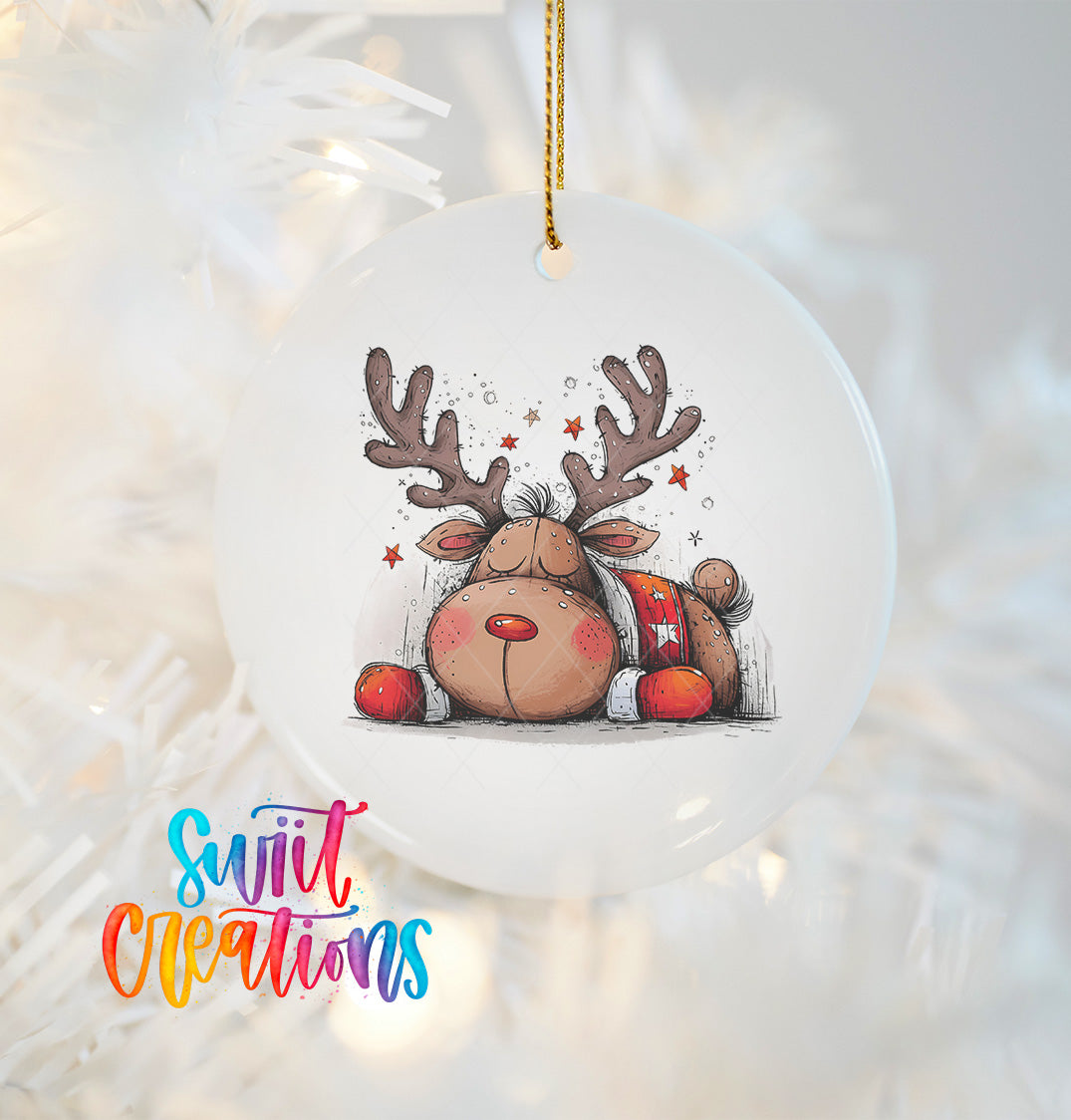 A white ornament with a cartoon image of a sleeping reindeer, surrounded by stars, hanging on a string.