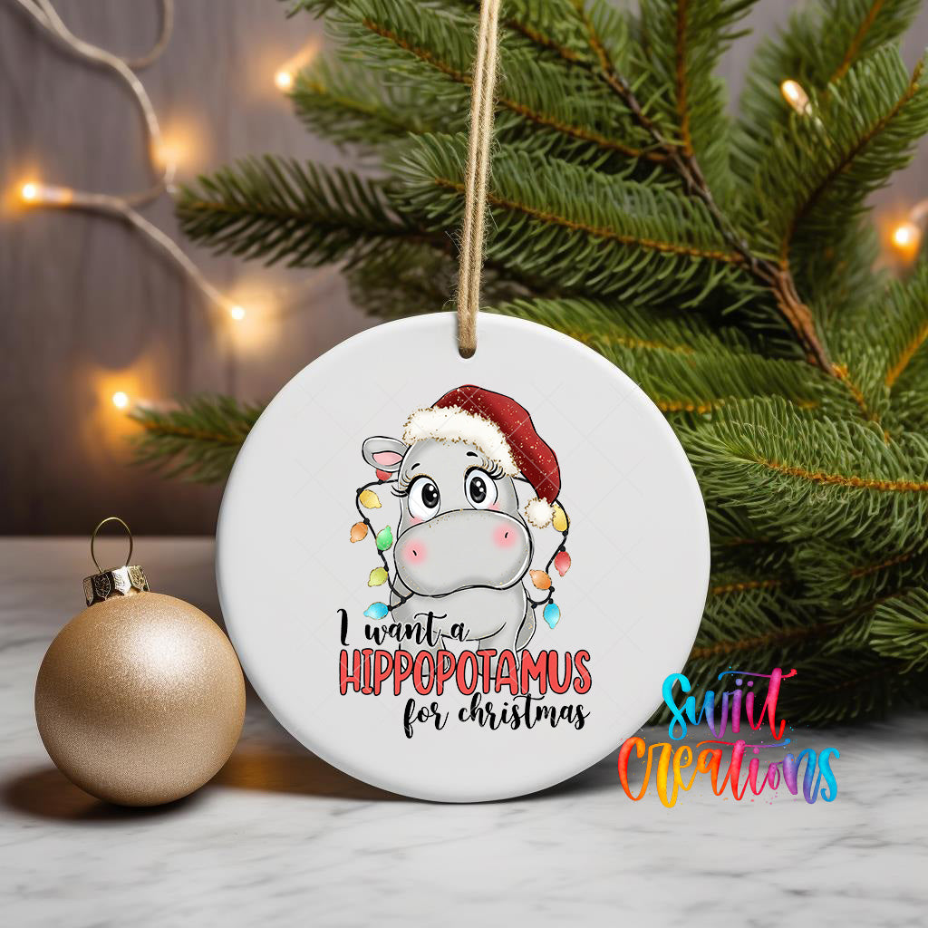 A white ceramic ornament with a cartoon image of a hippopotamus wearing a Santa hat, surrounded by Christmas lights and a pine tree.