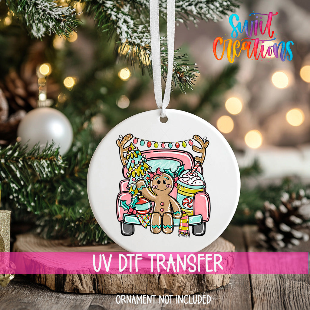 A white ornament with a gingerbread man and a truck, hanging on a Christmas tree.
