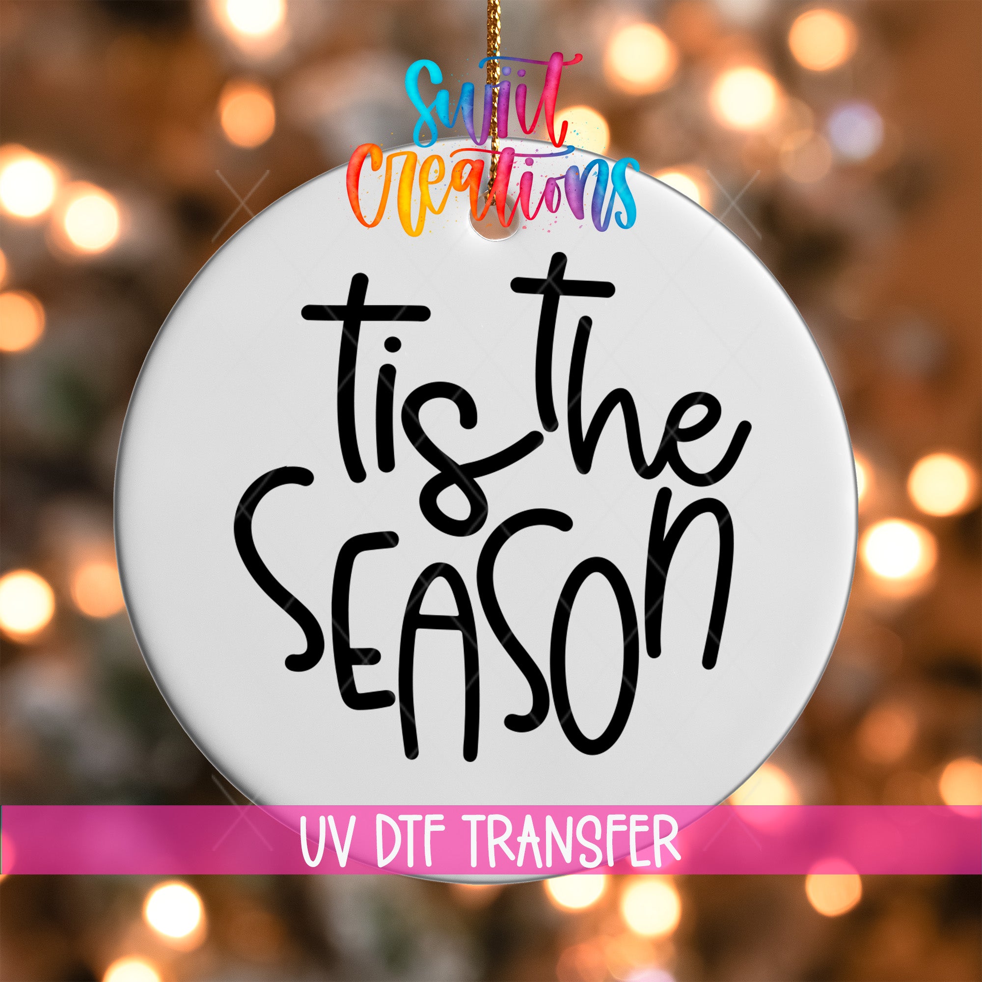 A white ornament with the text "Tis the SEASON" written on it, hanging against a background of colorful lights.