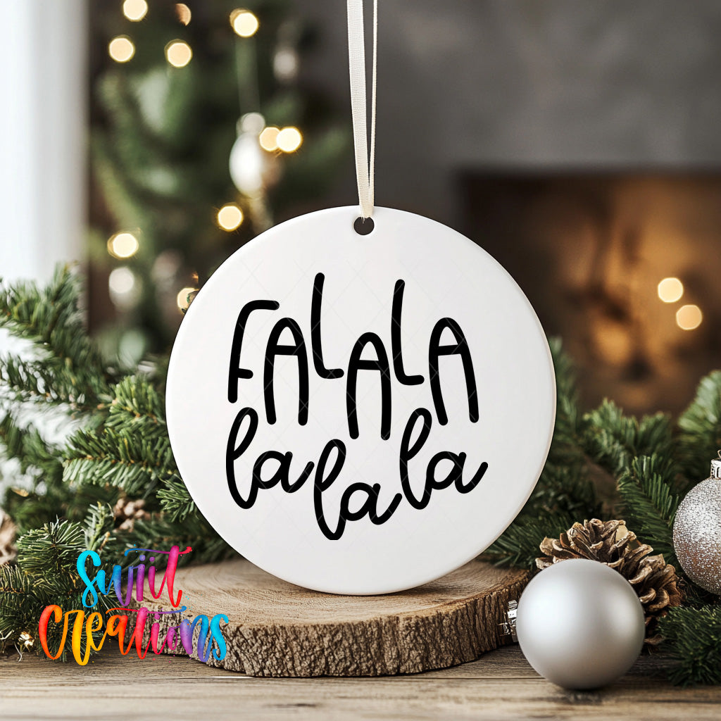 A white ornament with the text "FALA la la la" is displayed on a wooden surface, surrounded by Christmas decorations such as pine cones and ornaments.