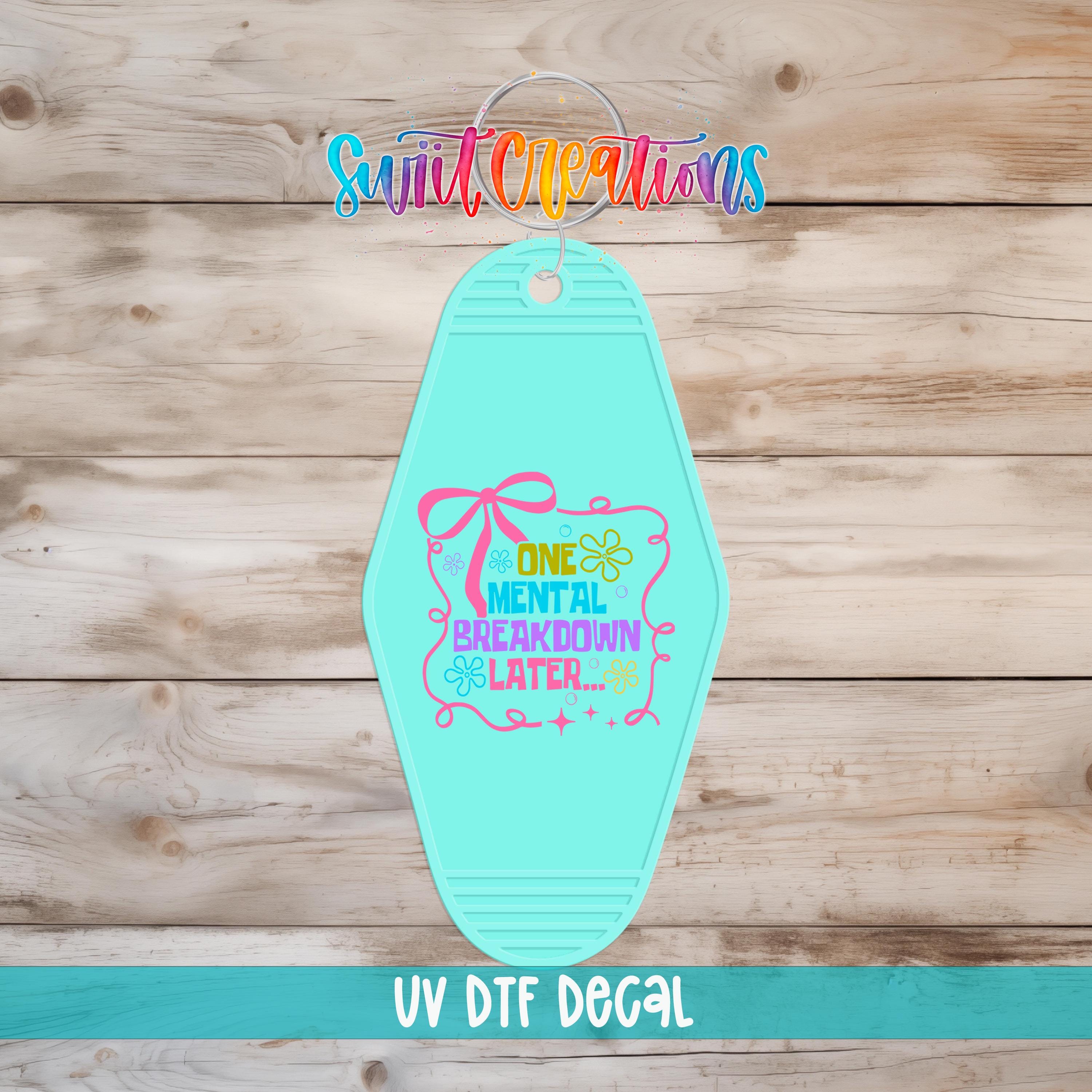 A turquoise keychain with a colorful graphic and text on it, placed on a wooden surface.