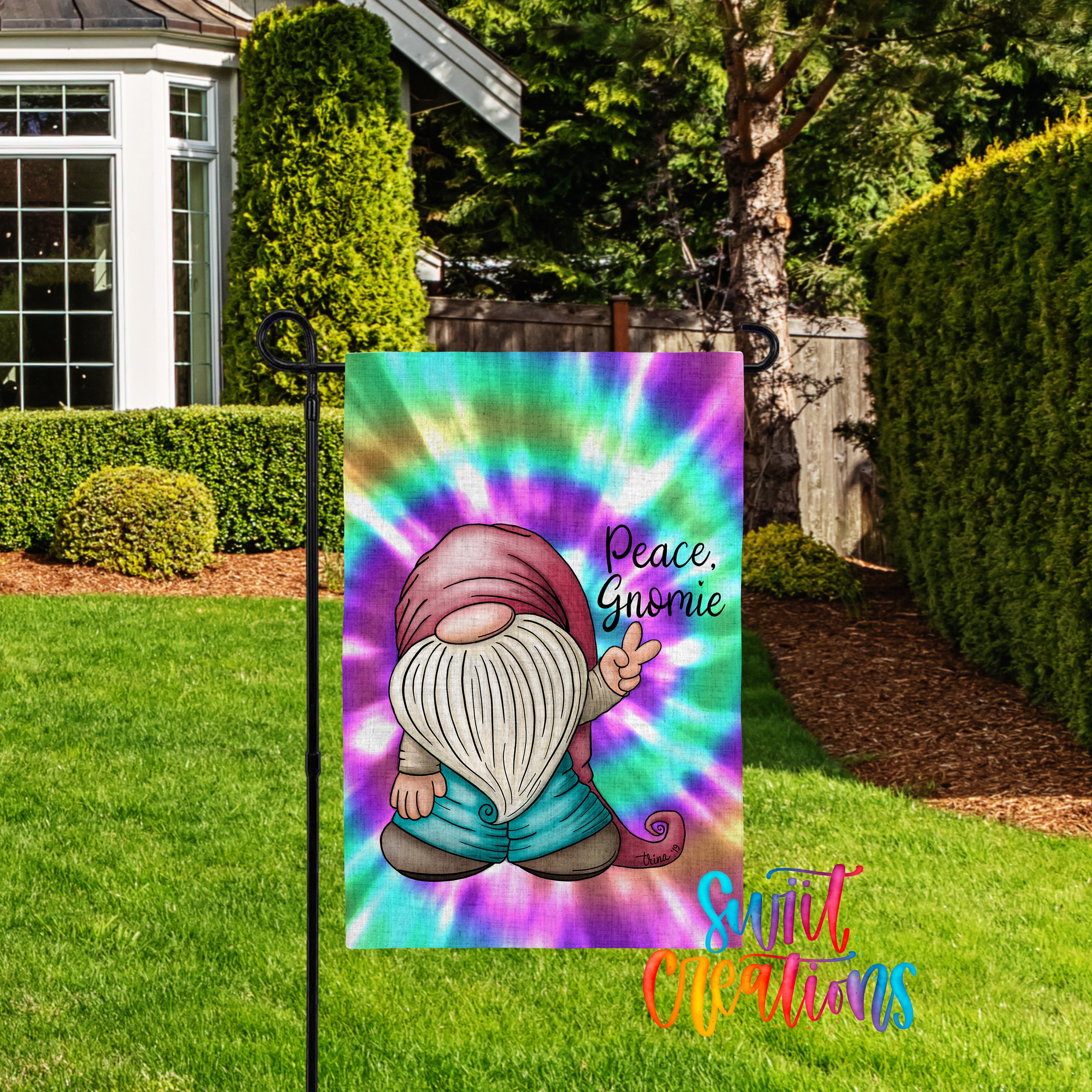 A colorful garden flag featuring a gnome character with a peace sign, set against a backdrop of a well-maintained lawn and trees.