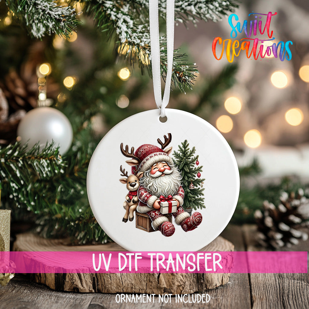 A white ornament with a Santa Claus and reindeer design hangs on a Christmas tree, surrounded by pine branches and other holiday decorations.