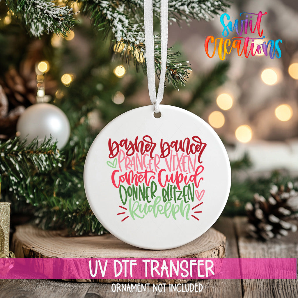 A white ceramic ornament with a colorful, hand-lettered design hangs on a Christmas tree.