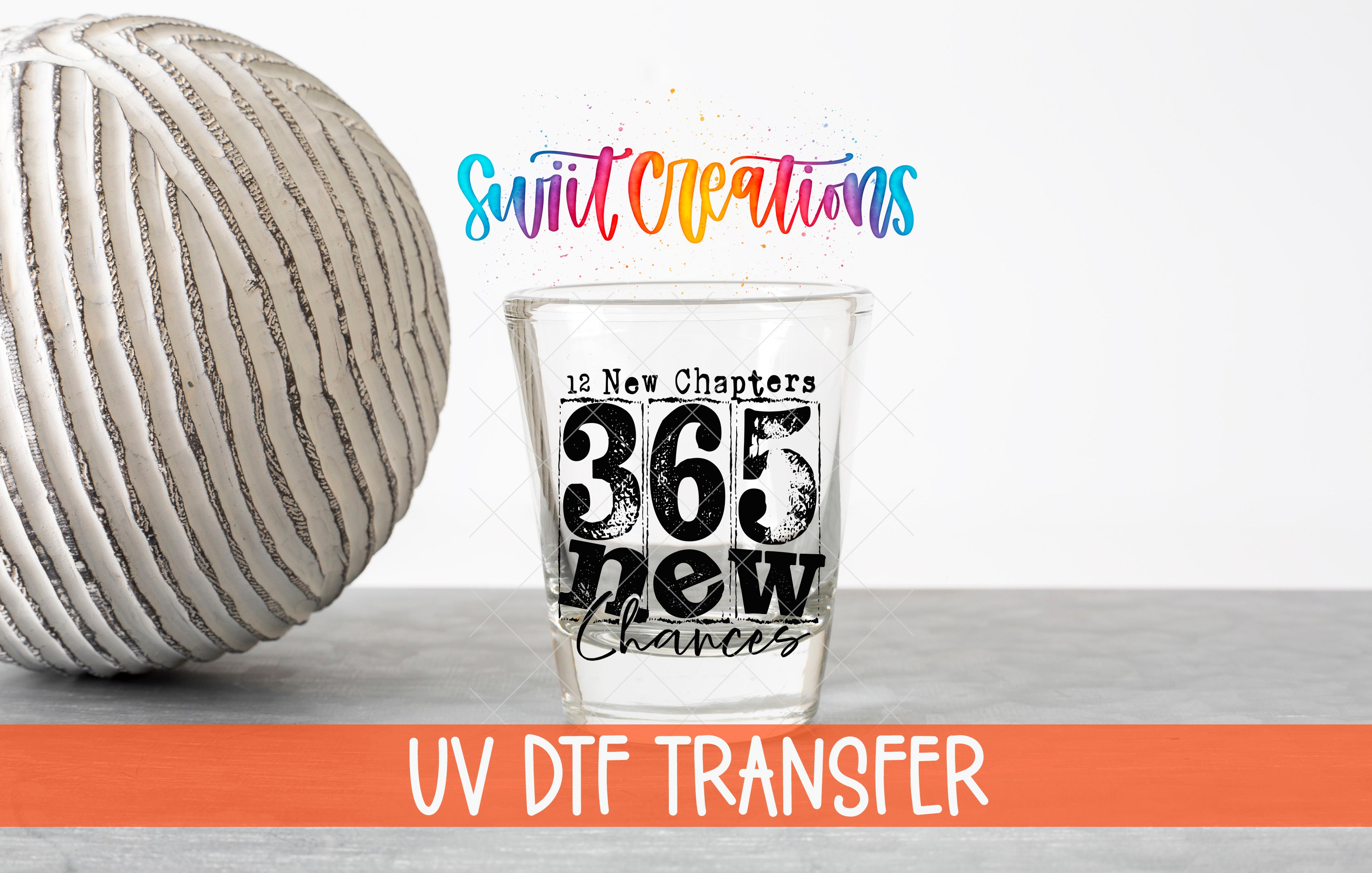 a glass with the text "365 New Chapters" and "UV DFT Transfer" printed on it, along with a colorful background that includes the text "Swit Creations" and "12 New Chapters".