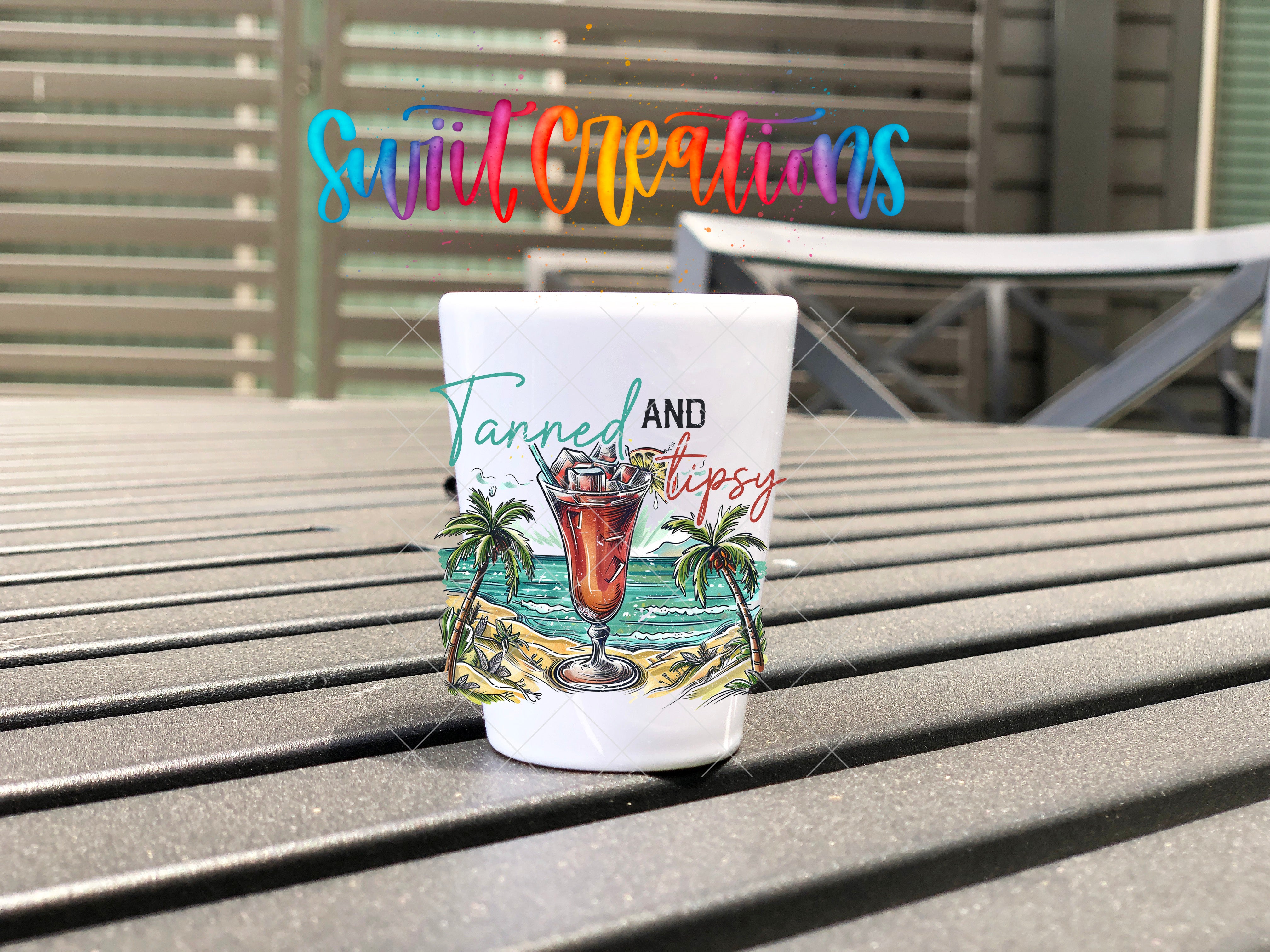 A colorful mug with a tropical beach scene and a drink in it, placed on a wooden surface.