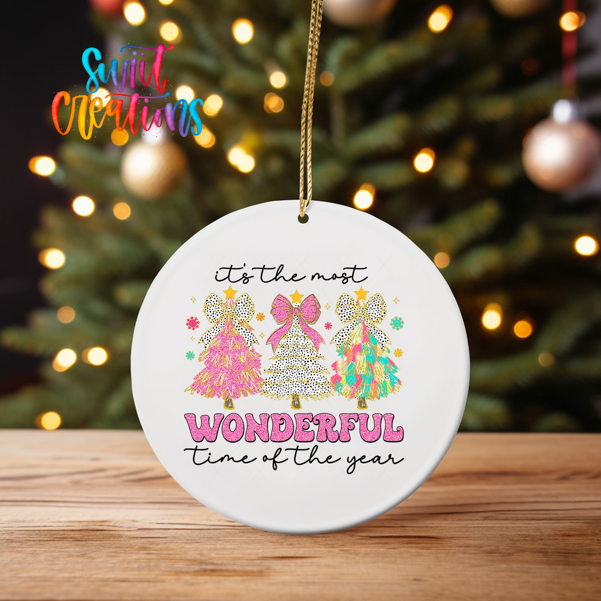 A white ceramic ornament with a festive design hangs on a wooden surface, featuring a Christmas tree and the text "It's the most WONDERFUL time of the year" in a playful font.