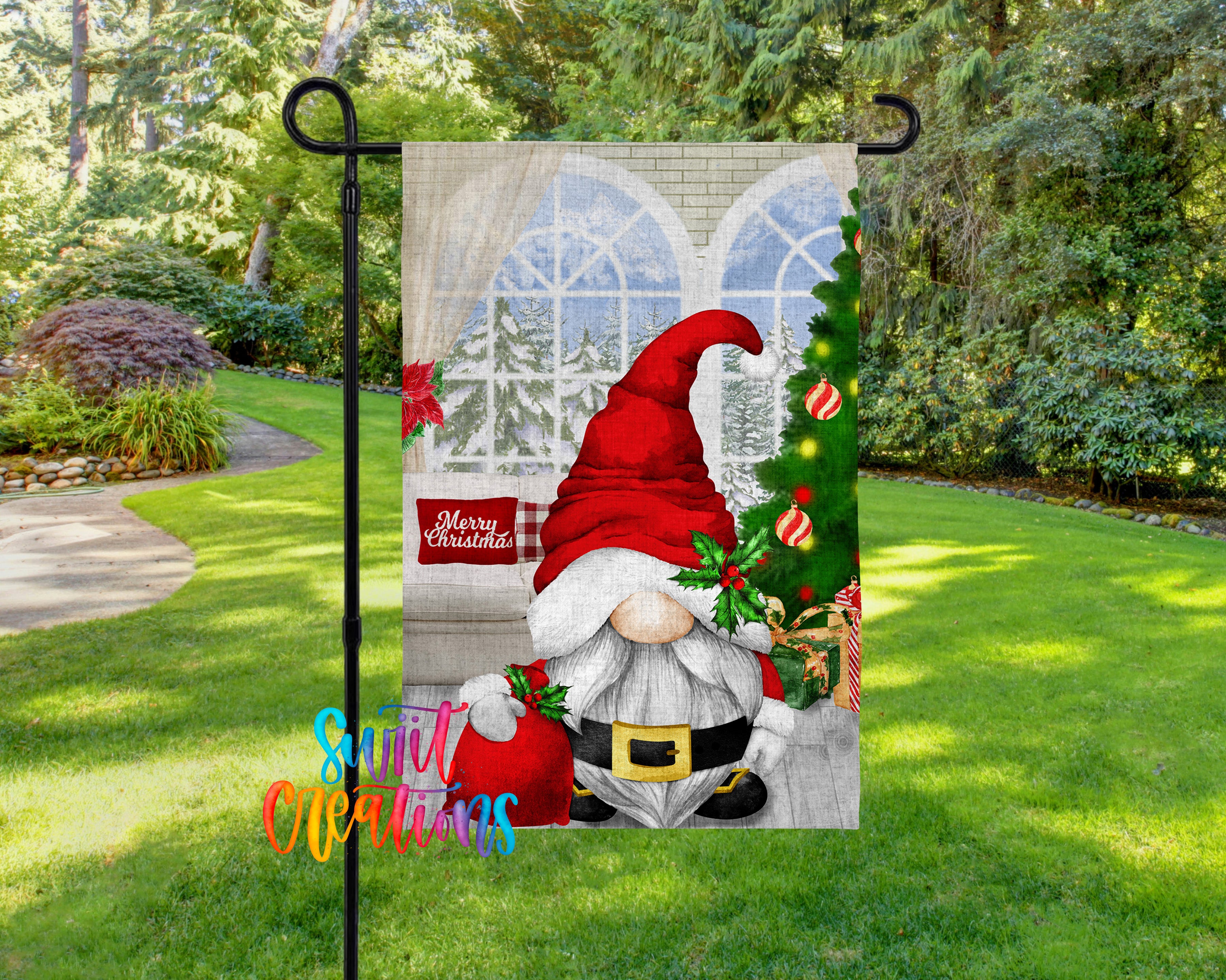 A Christmas-themed garden flag featuring a gnome wearing a red hat and holding a Christmas tree, with a snowy landscape and trees in the background.
