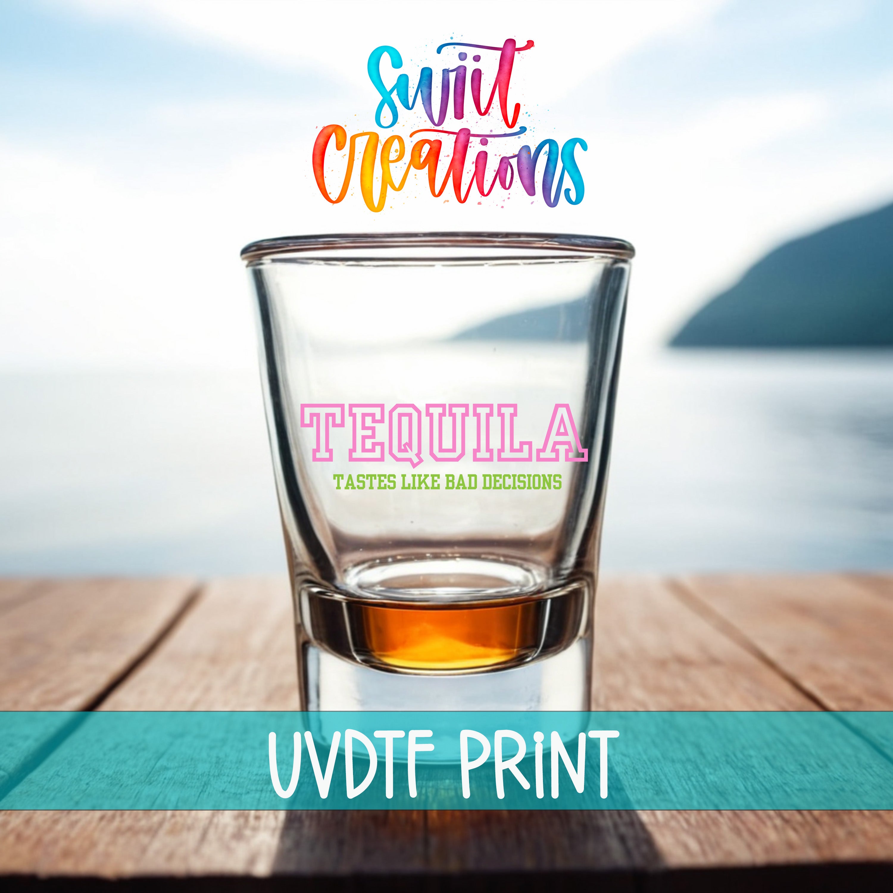 A clear shot glass filled with a golden liquid, placed on a wooden surface with a scenic view of a body of water and mountains in the background.