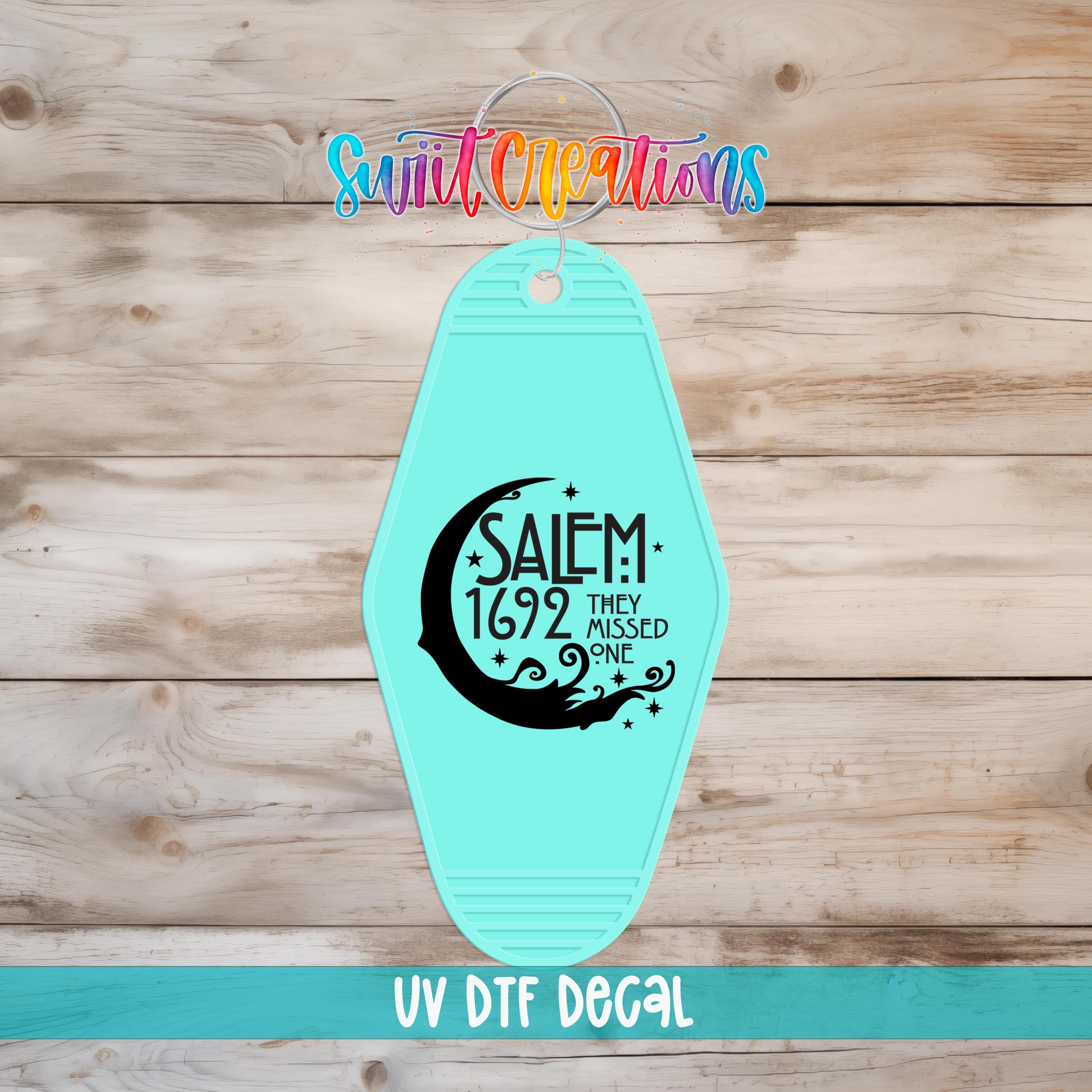 A turquoise keychain with a black and white design and text, placed on a wooden surface.