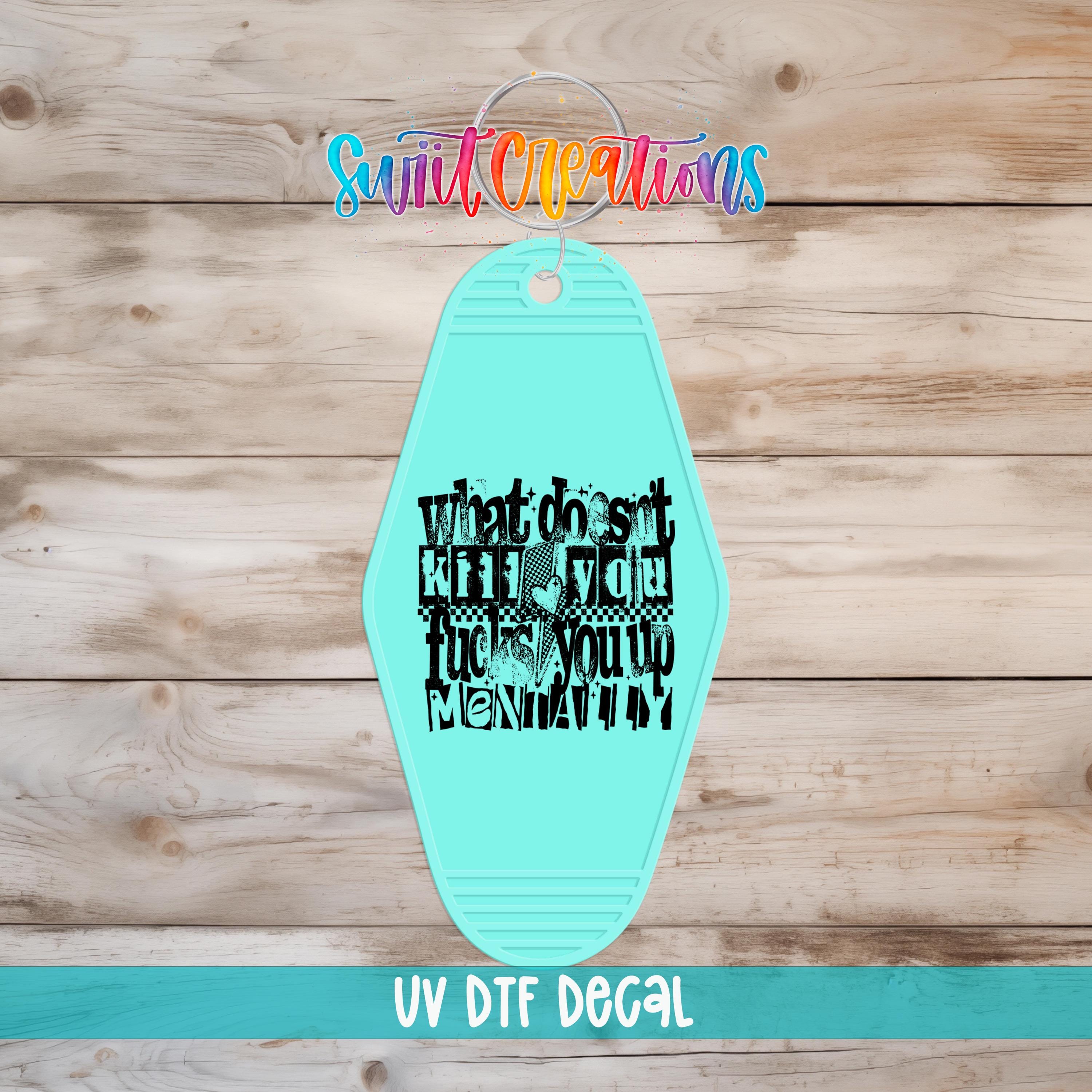 A turquoise-colored keychain with the text "What does it mean to kill someone" printed on it, displayed on a wooden background.