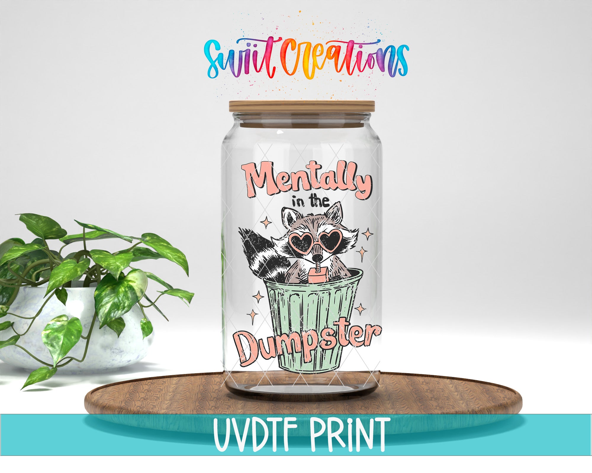 A glass jar with a raccoon wearing sunglasses and the text "Mentally in the Dumpster" printed on it, placed on a wooden surface.