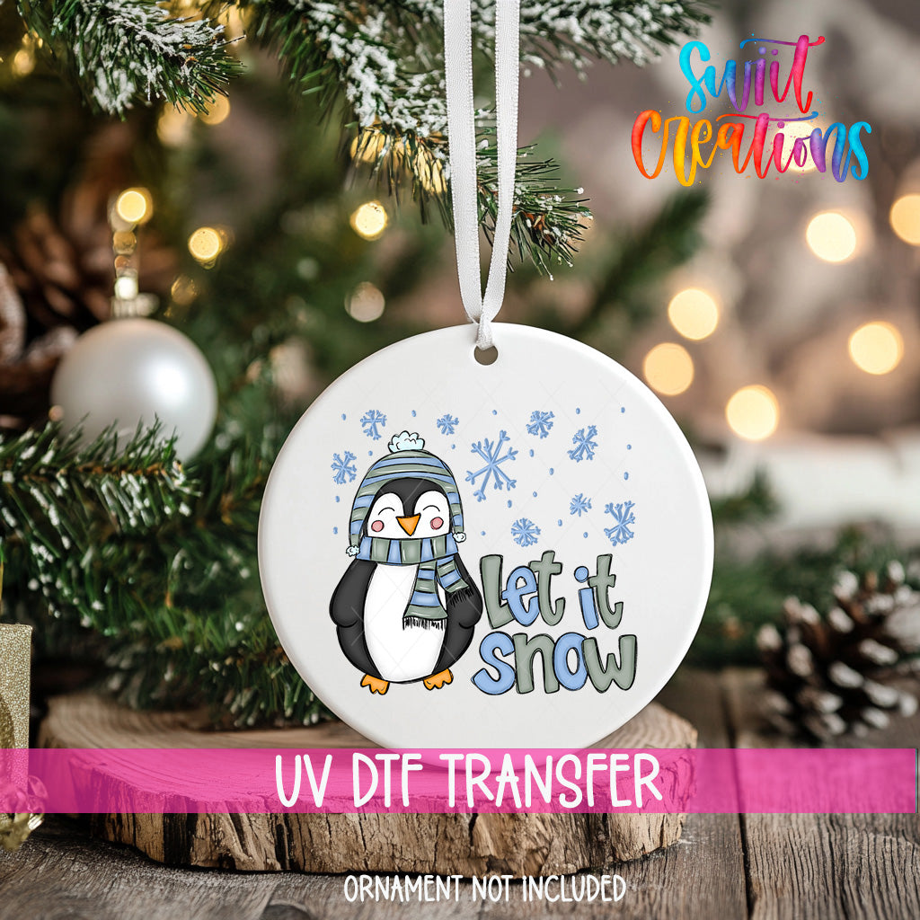 A white ornament with a penguin and snowflakes hanging on a Christmas tree.