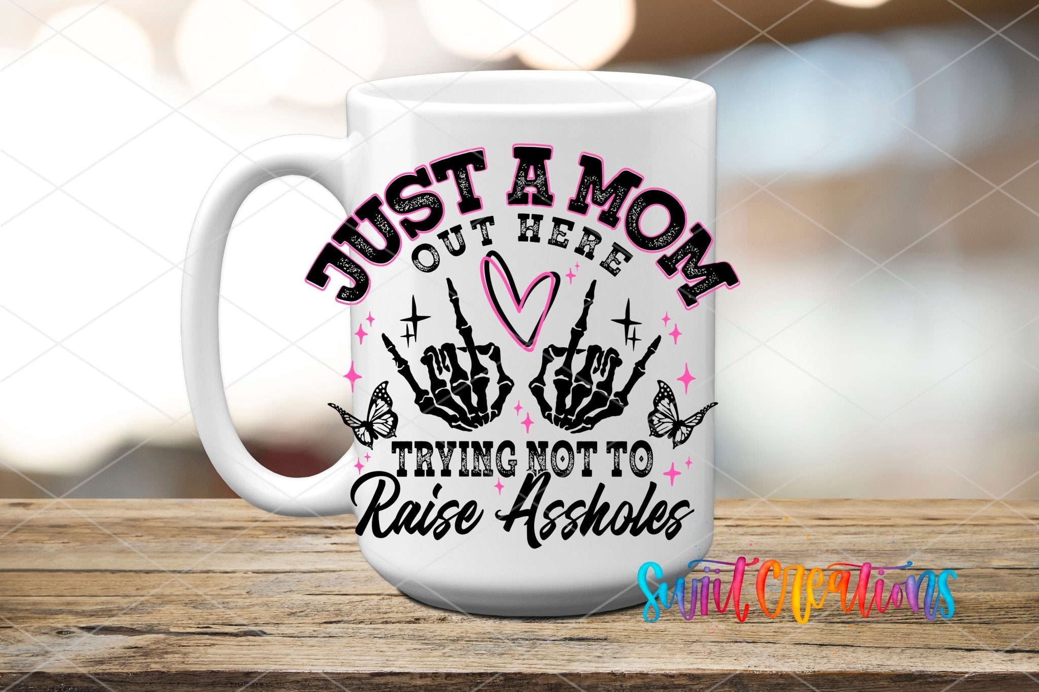 Just a Mom Trying Not To Raise Assholes UV DTF transfer displayed on a white ceramic mug from Swiit Creations