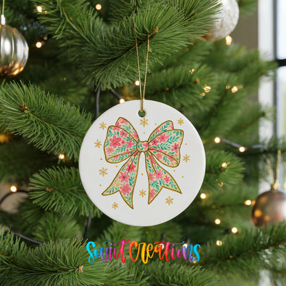 A white ceramic ornament with a floral design and a gold bow is hanging on a Christmas tree.