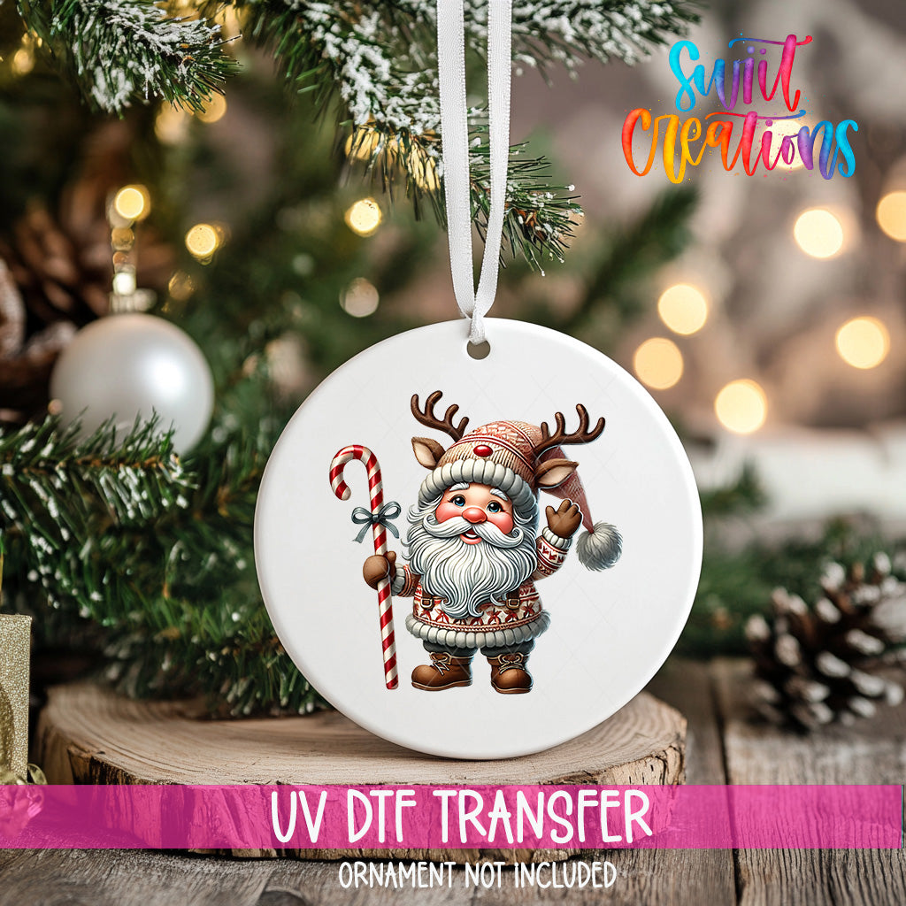 A white ornament featuring a cartoon Santa Claus holding a candy cane and reindeer is hanging on a Christmas tree.