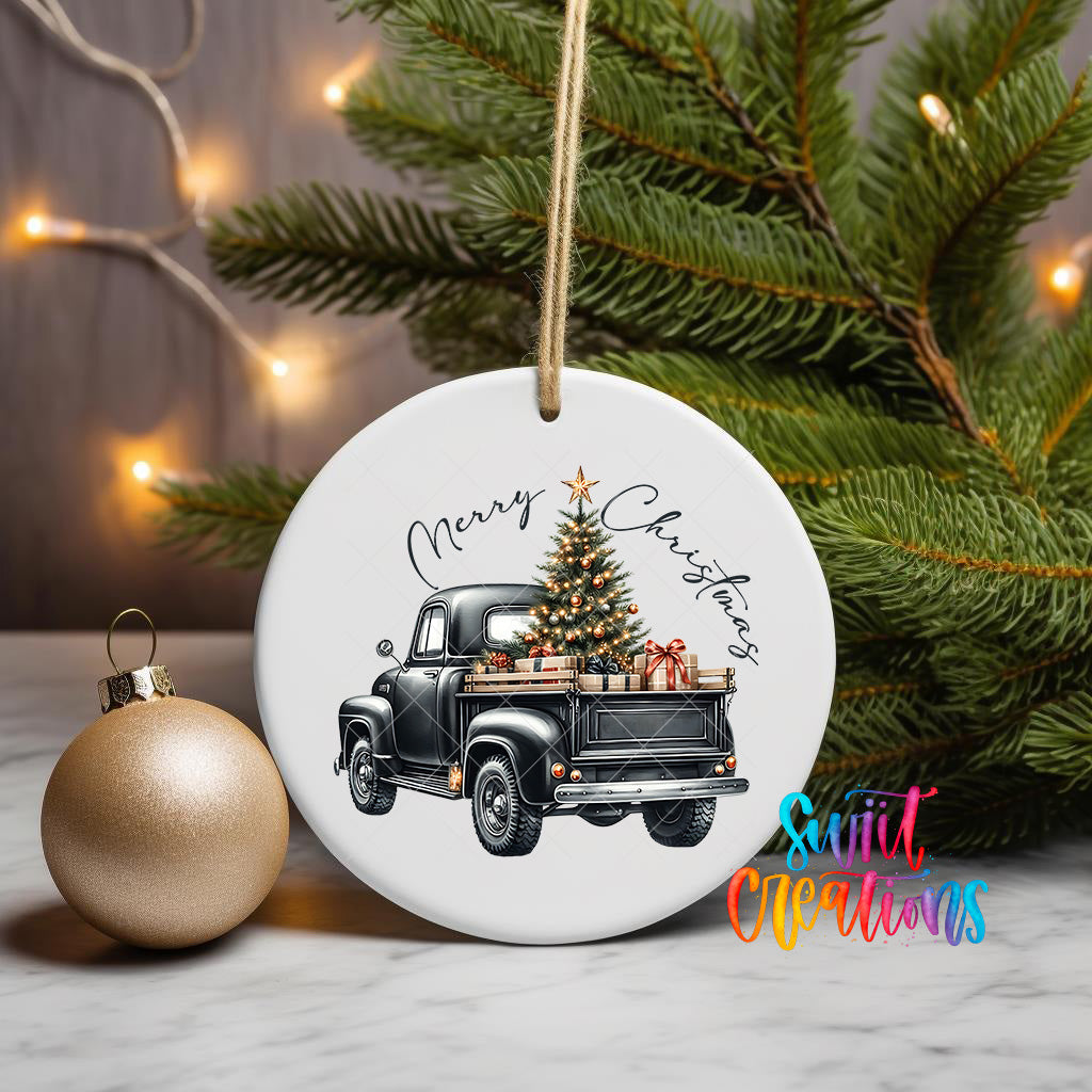 A white ceramic ornament featuring a black vintage truck with a Christmas tree in its bed, surrounded by lights and greenery.