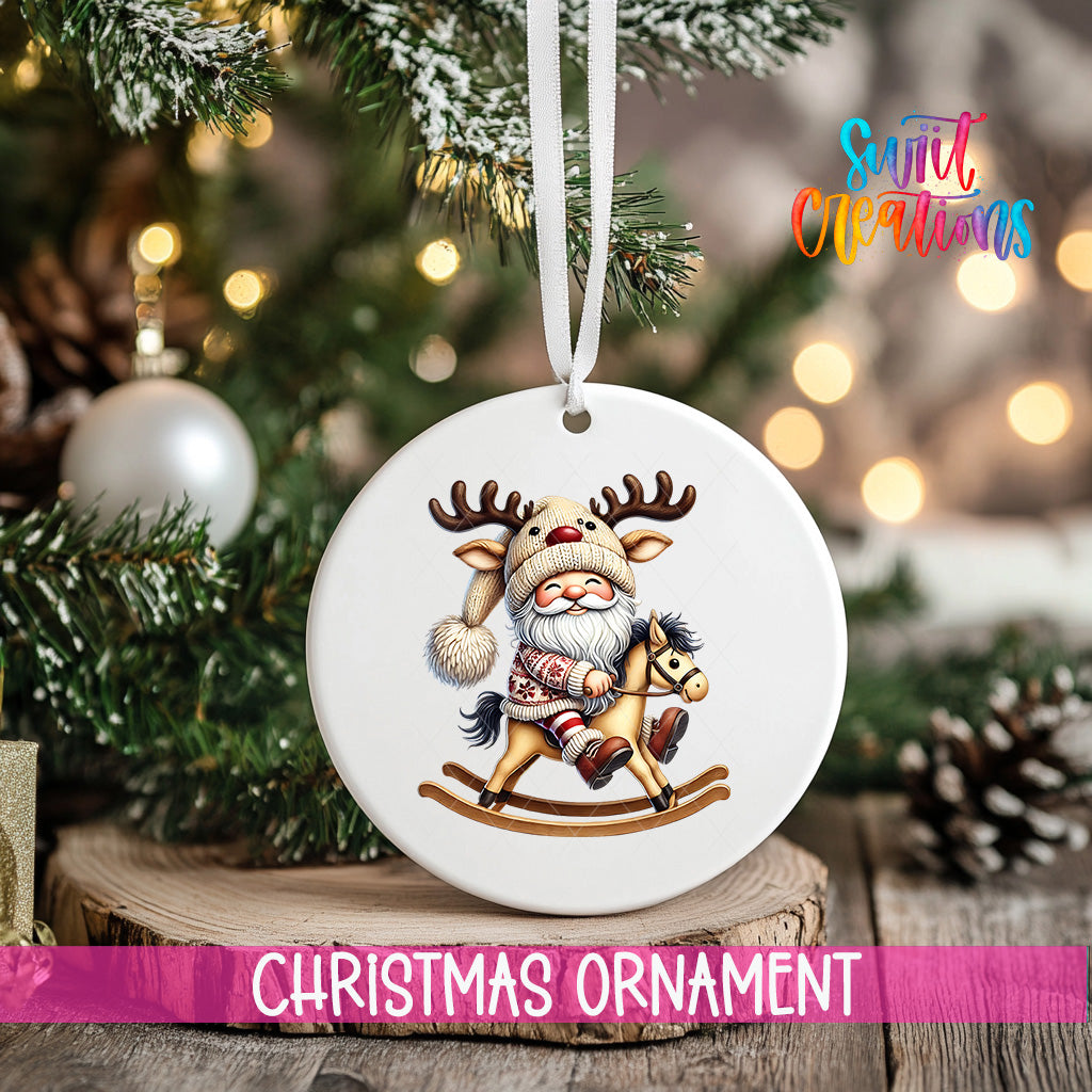 A white Christmas ornament featuring a Santa Claus figure riding a rocking horse, with a pine tree and twinkling lights in the background.