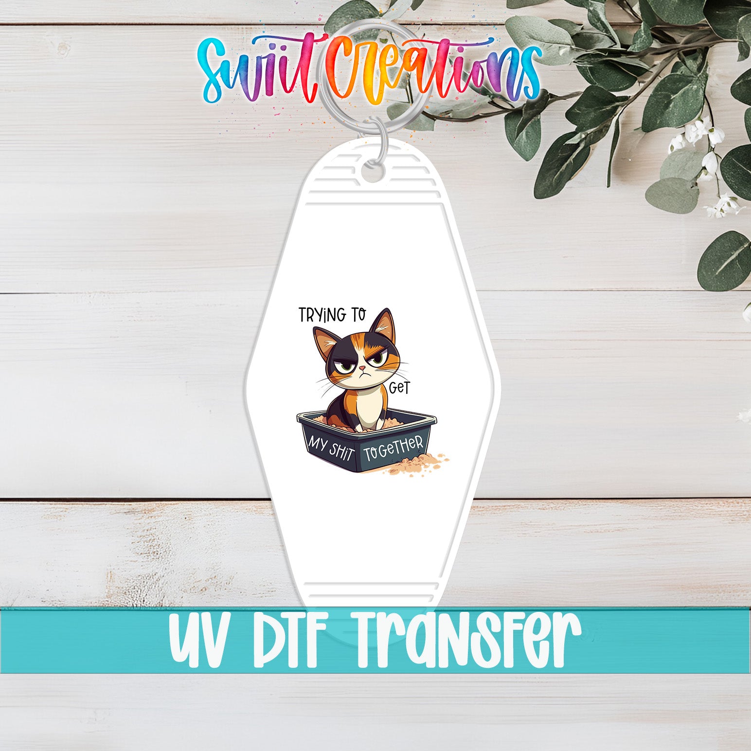 A keychain with a cartoon cat and the text "Trying to get my shit together" printed on it, along with a UV DFT transfer label.