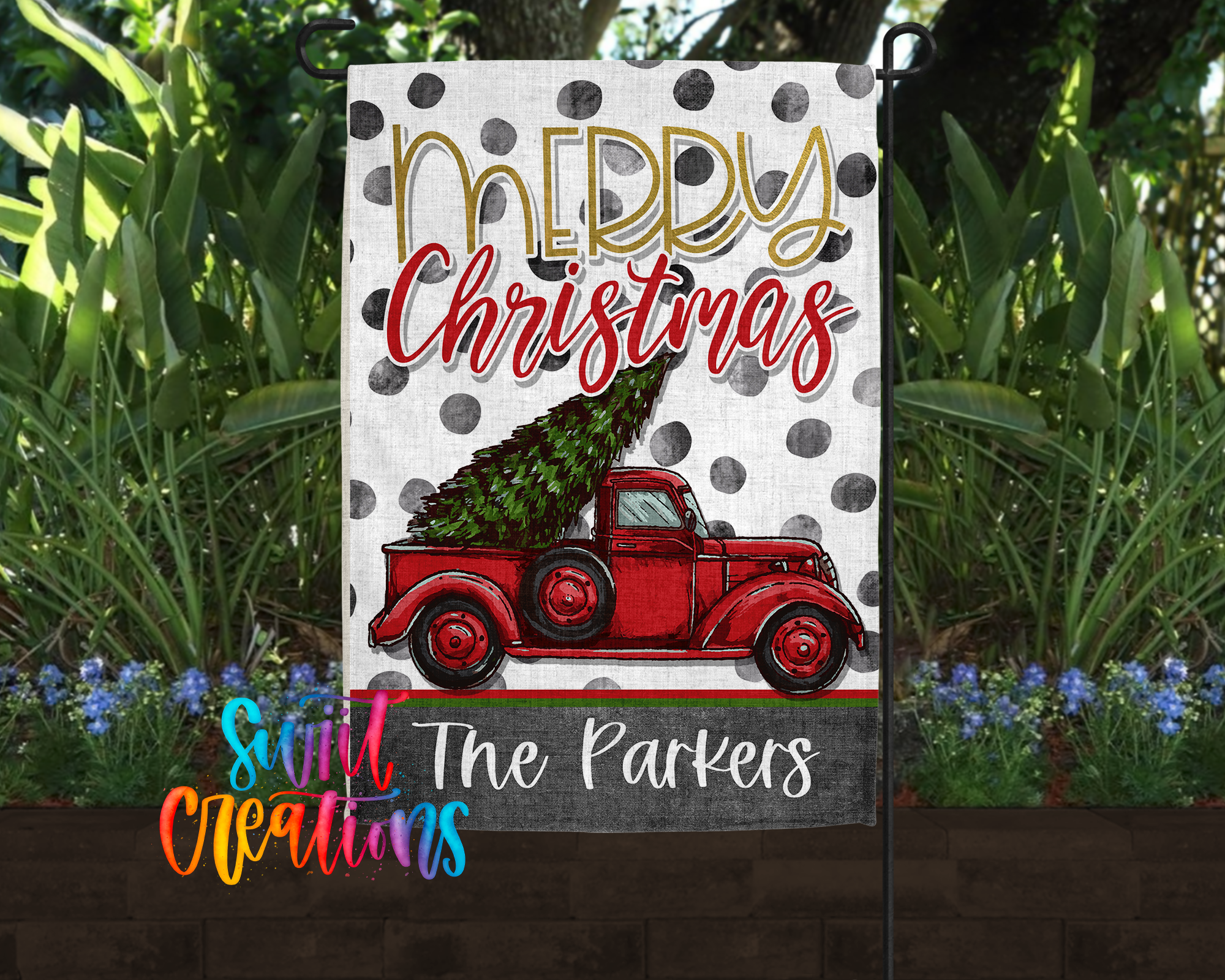 A Christmas-themed flag with a red truck carrying a Christmas tree, surrounded by greenery and flowers.