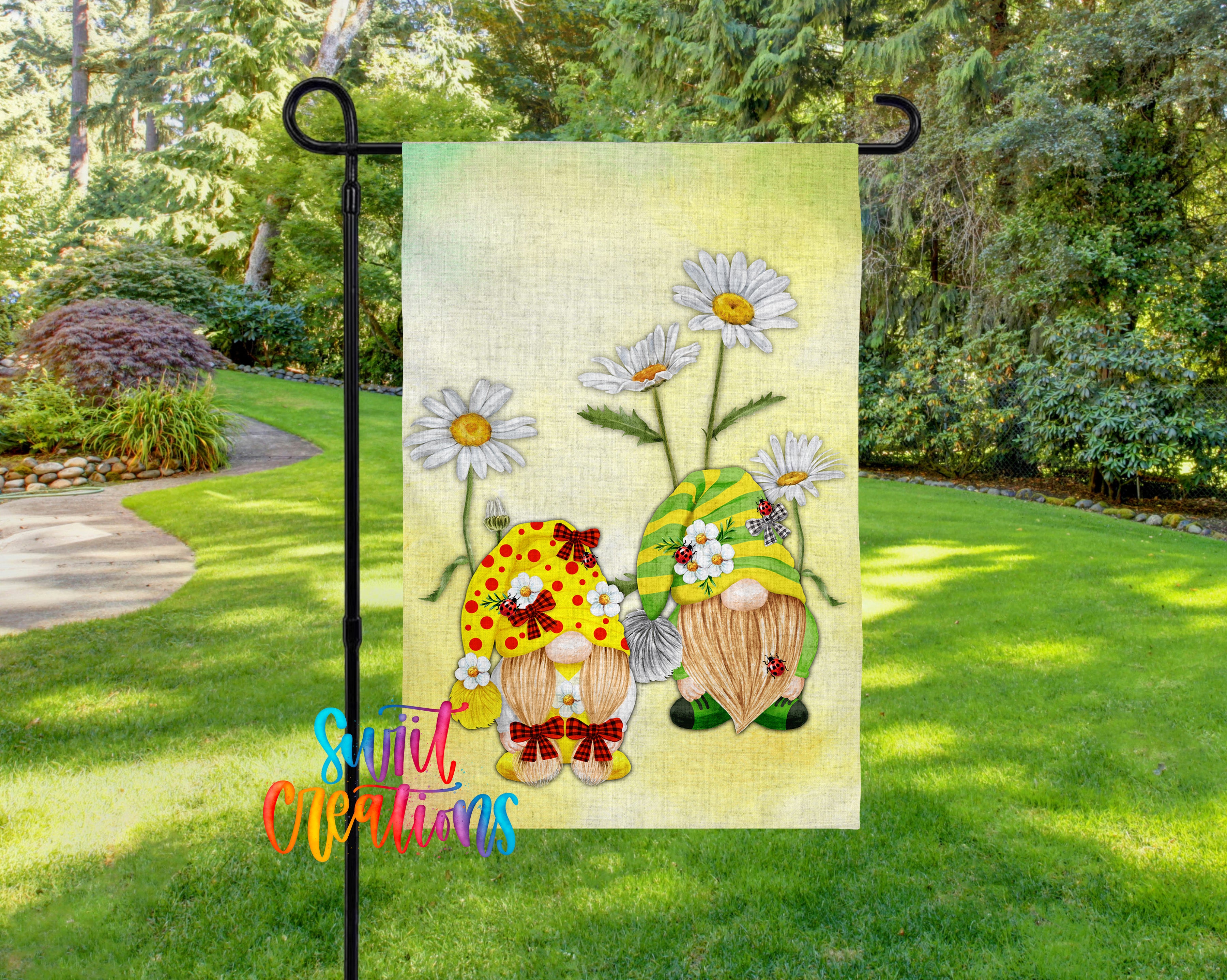 A garden flag featuring two gnomes with flower crowns, surrounded by daisies, set against a backdrop of lush greenery.