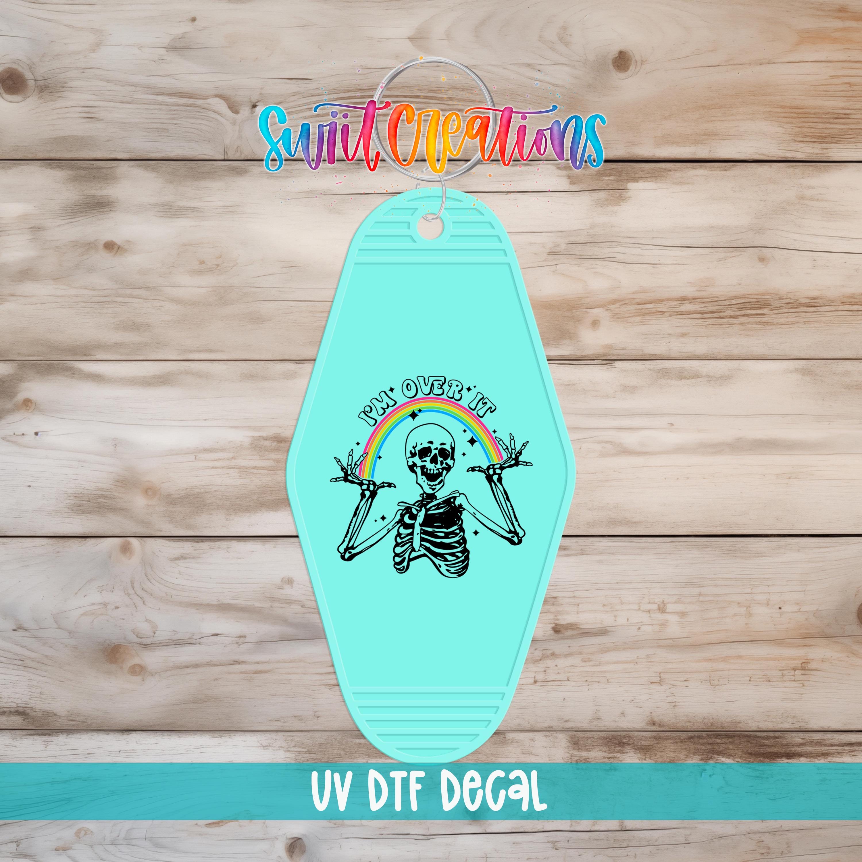 A turquoise keychain with a skeleton graphic and a rainbow graphic, along with the text "UV Dtf Decal"