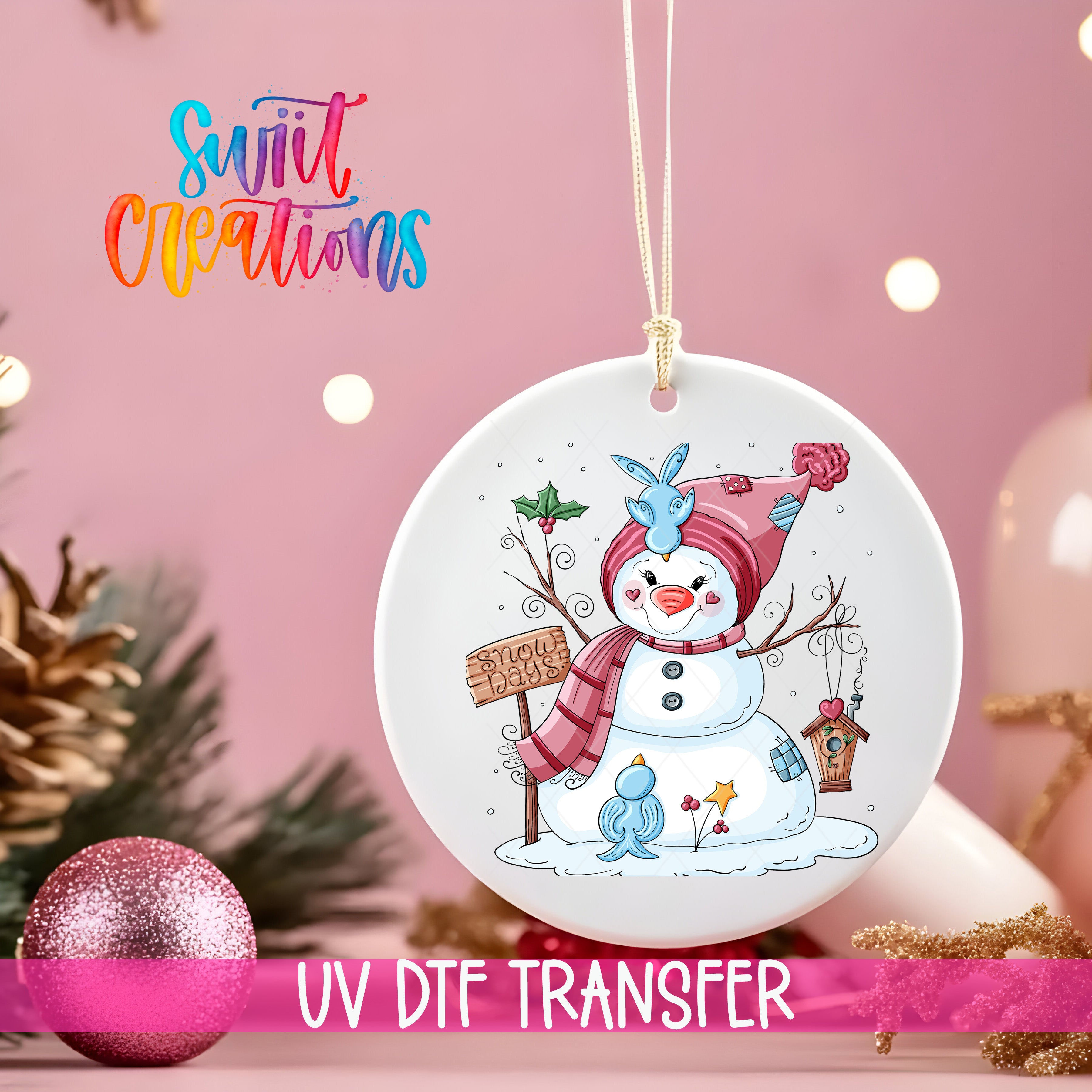 A white ornament with a snowman and a sign, hanging on a string against a pink background.