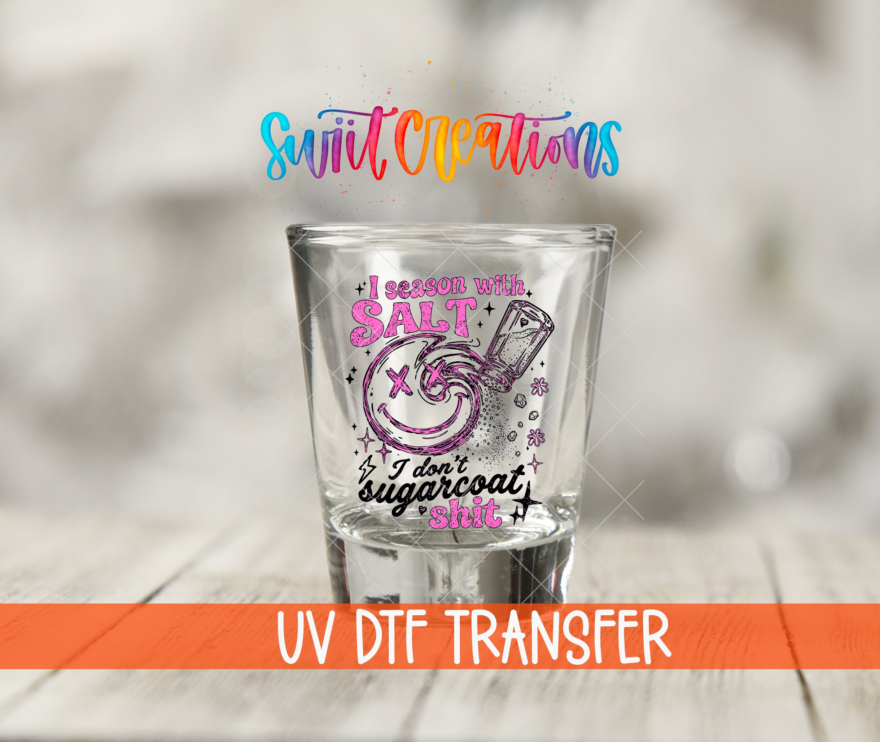 A shot glass with a colorful design and text printed on it, placed on a wooden surface.