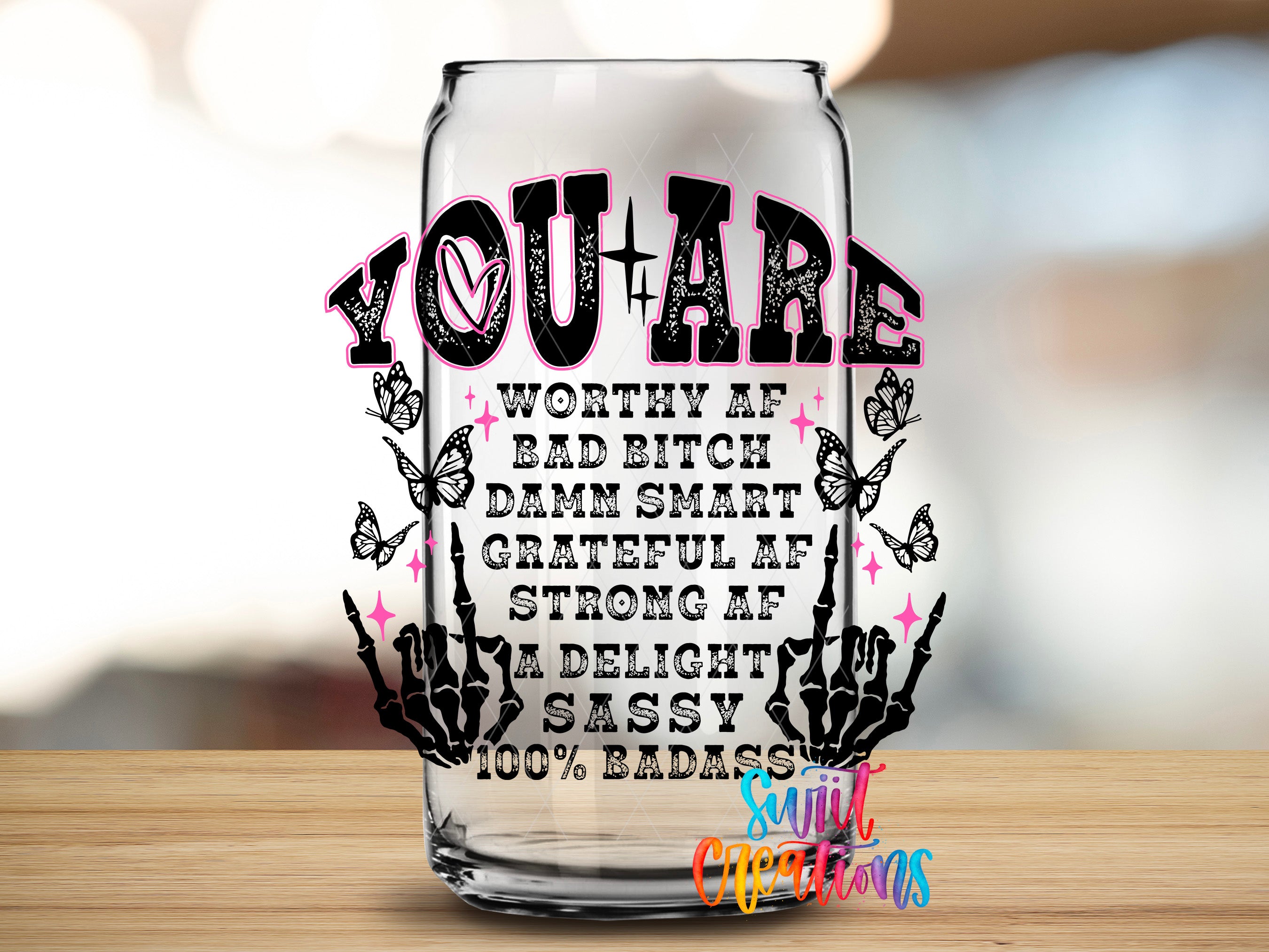 a glass with a message that reads "YOU ARE WORTHY AF BAD BITCH DAMN SMART GRATEFUL AF STRONG AF A DELIGHT SASSY 100% BADASS" along with a skeleton hand gesture.